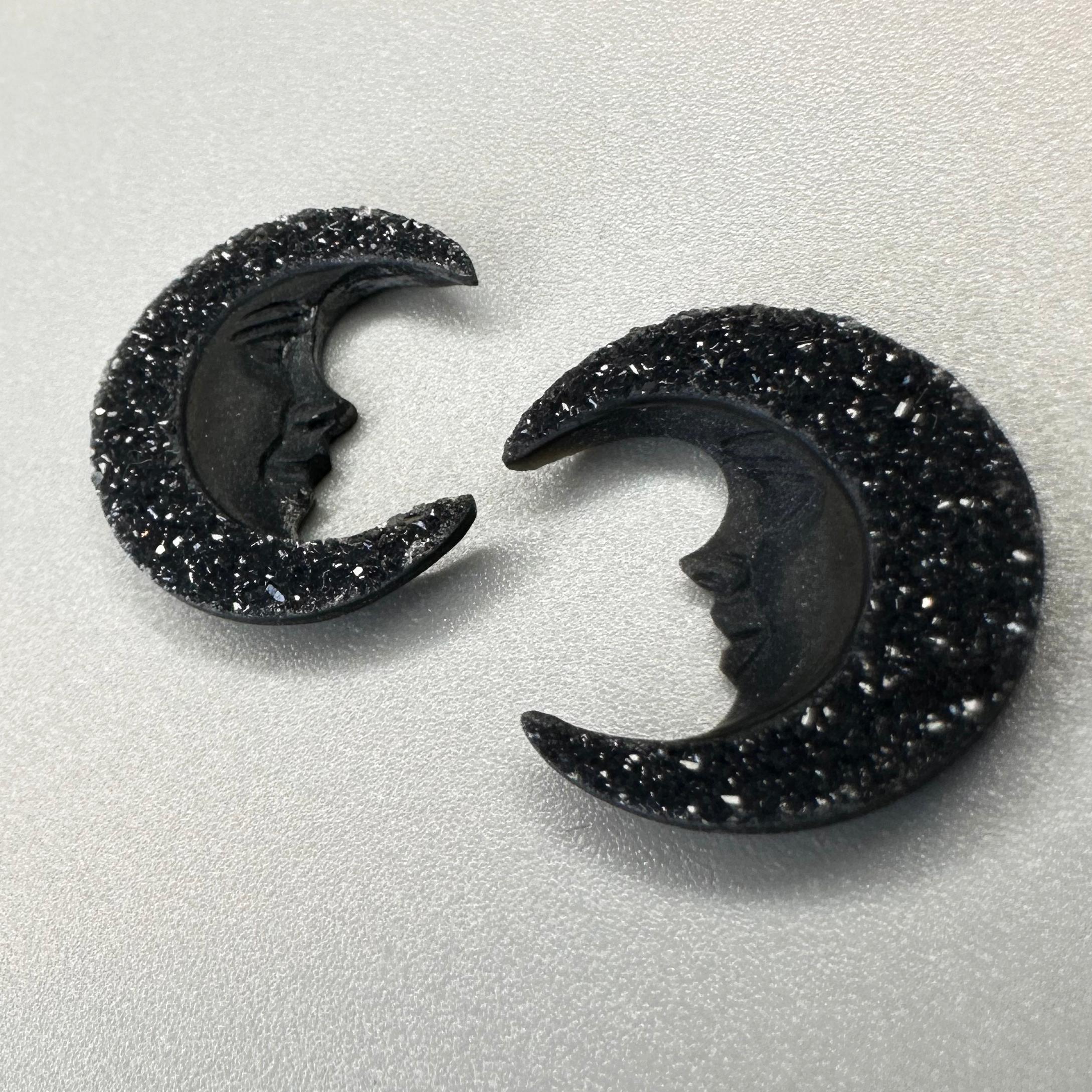 Step into the moon's shadow and catch a glimpse of their complementary faces haloed in sparkling stars and immortalized in this beautifully carved gem set. 

This stunning pair of black druzy agate moon faces were hand crafted by the master carvers