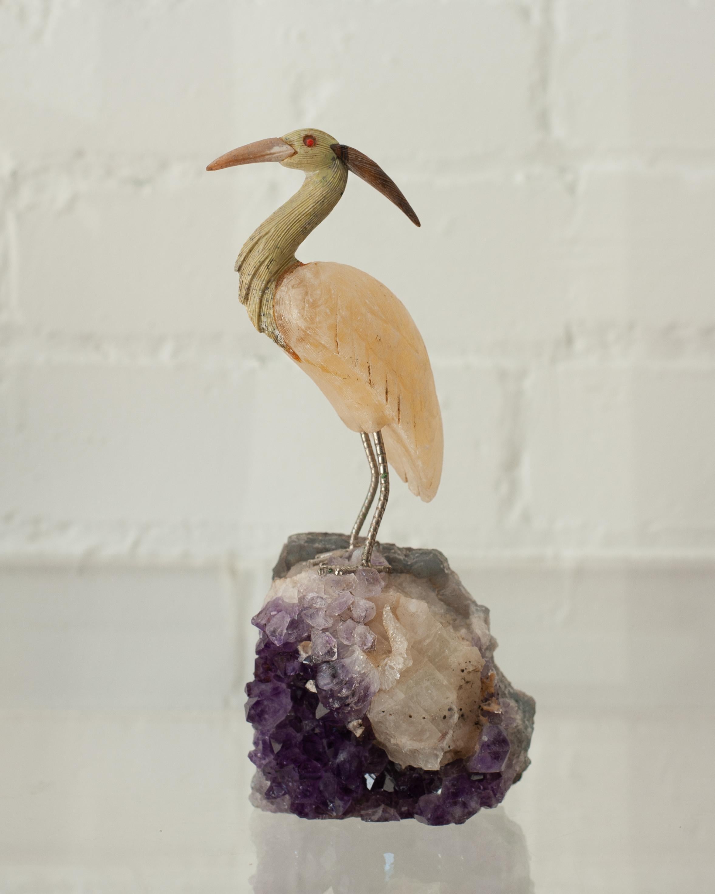 A beautiful hand carved semi precious stone crane mounted on an amethyst mineral specimen base. This exotic bird is a decorative combination of ornithology and geology.