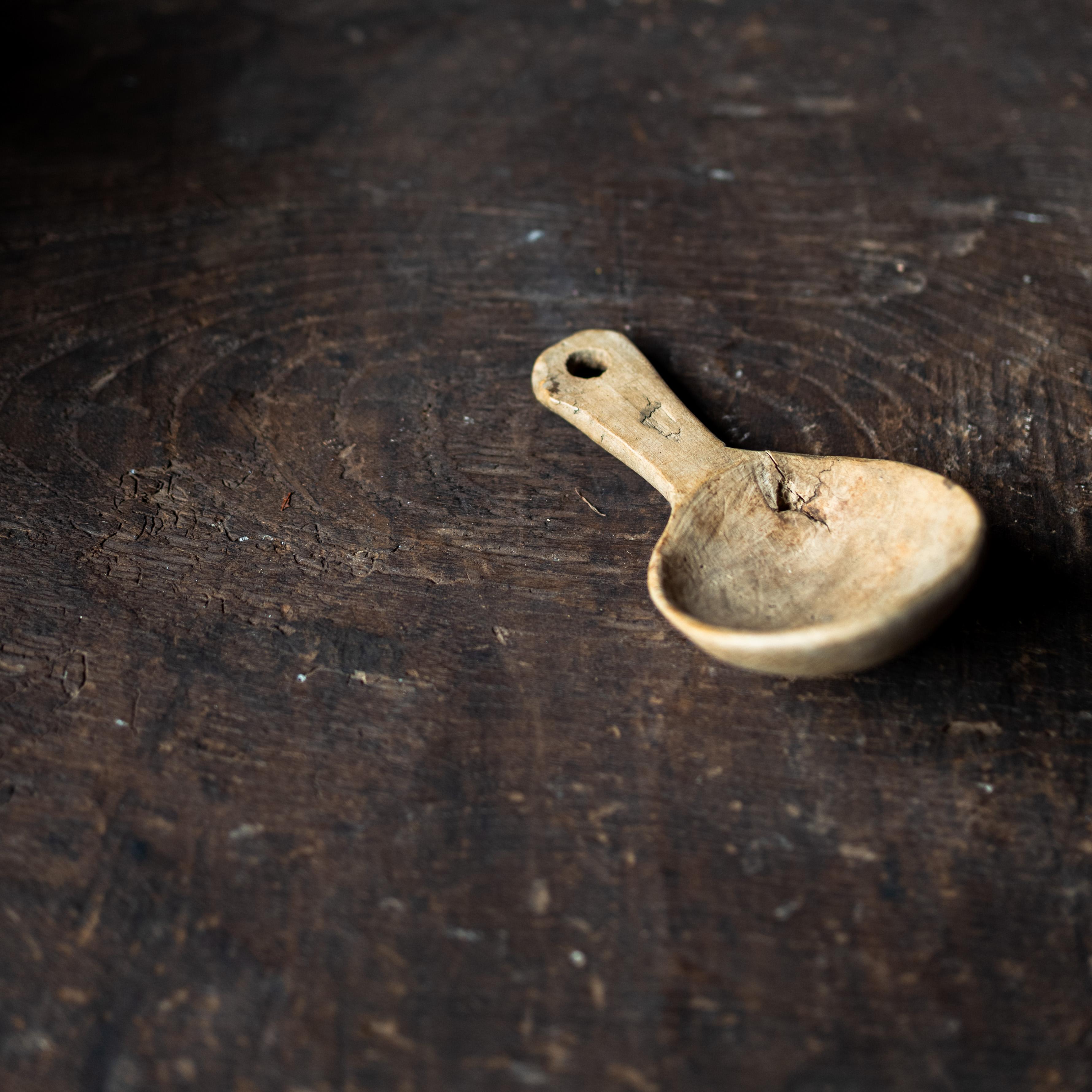 Questo cucchiaio rustico in legno intagliato a mano emana carattere e storia. La sua forma semplice e utilitaria è arricchita da decenni di utilizzo, con un manico liscio e una ciotola profonda modellata da strumenti manuali. Un piccolo foro