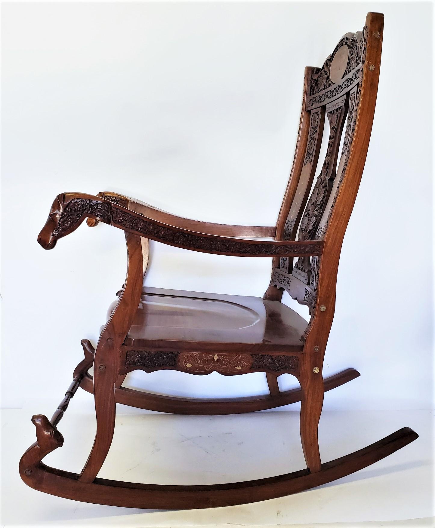 Hand carved oak rocking chair with beautiful ornate floral design with hand carved camel arm ending. There is a beautiful brass inlay through out the design that adds a subtle and extravagant touch to the aesthetic value of the rocking chair.