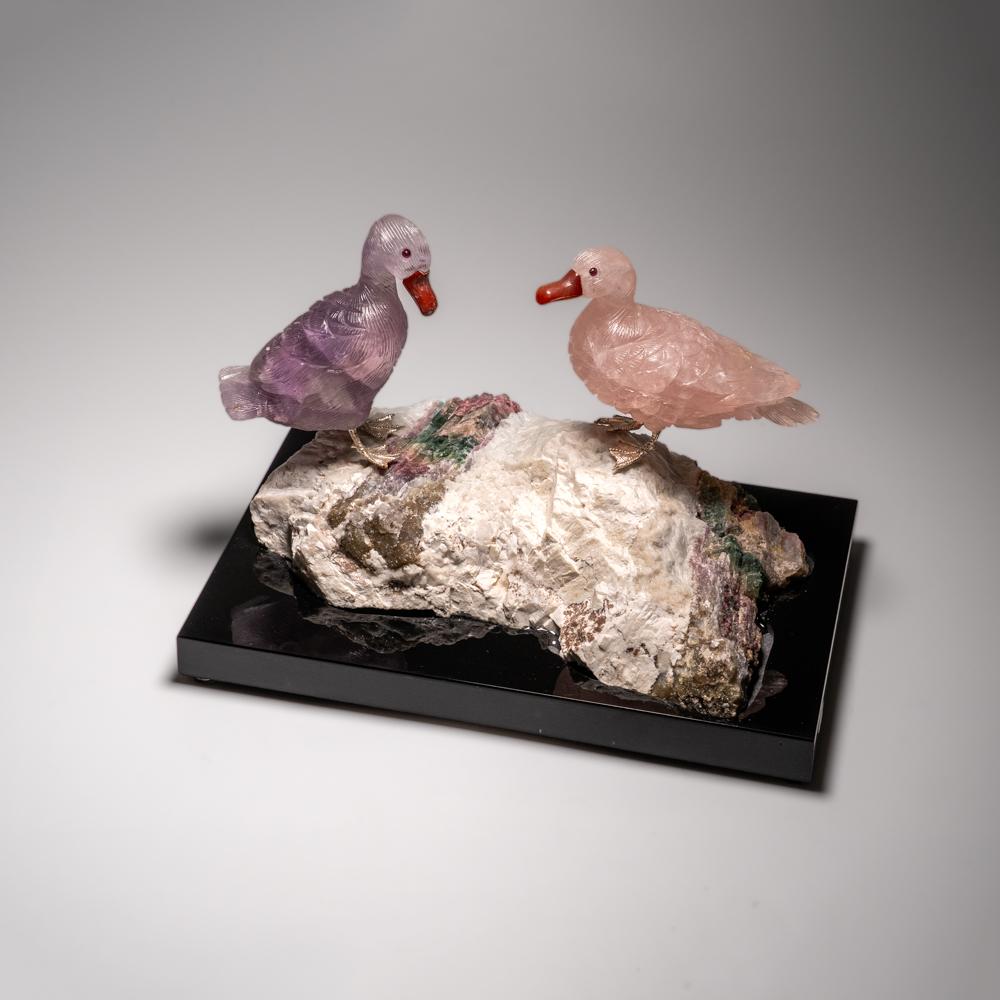 This Duck carving is a unique piece of art, carved from museum-quality fluorite and rose quartz with onyx eyes and a carnelian beak. The ducks are perched atop a green tourmaline in albite matrix and mounted on a custom stand for convenient display.