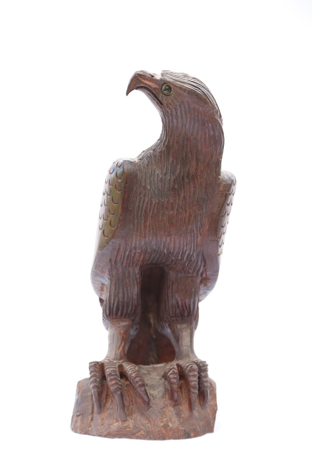 Hand carved eagle, of rosewood, perched upon rockery, with glass eyes. Highly stylized bird-of-prey with exaggerated angular beak, head and large talons. 

Stock ID: 1902.