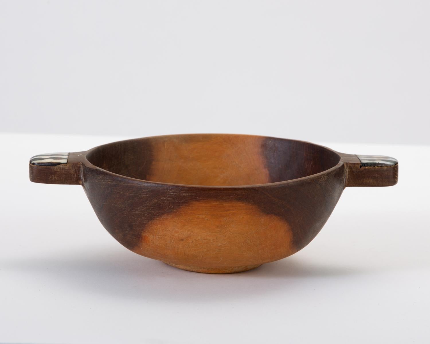 A handmade African sandalwood bowl with handles in a rough-hewn style. A wide band of contrasting sapwood lends a well-chosen symmetry to the overt rusticity of the traditional design. The handles are notched to accommodate the inset bone accents,