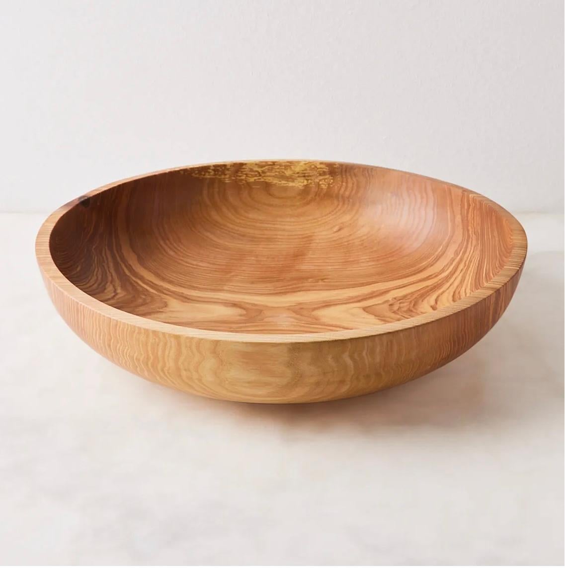 This large wooden bowl is a real showstopper. Hand-carved from a single piece of ash wood, it was made to become a perfect vessel for your dining table. A beautiful color gradient starts with a very light beige shade and goes as far as deep