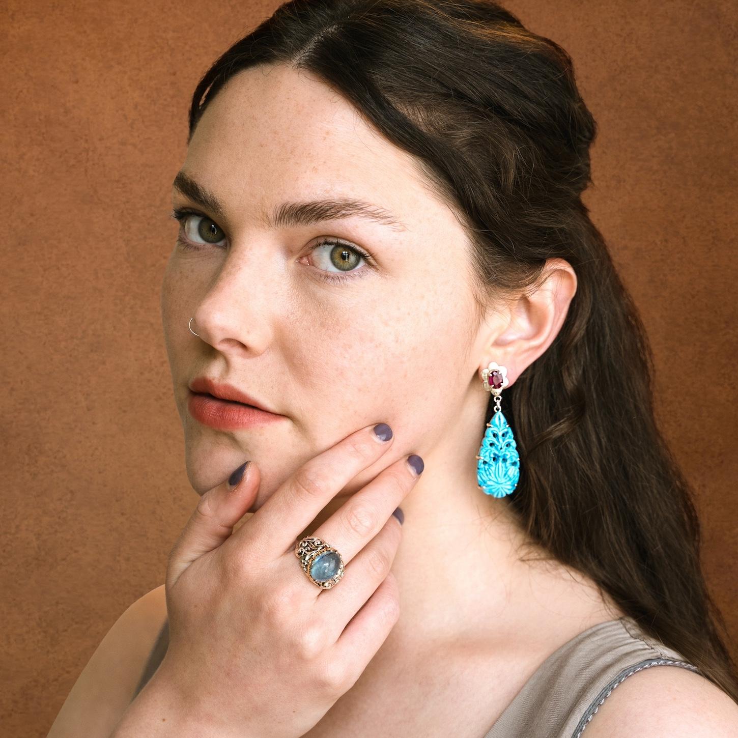 These stunning one-of-a-kind turquoise ruby earrings have been handmade in our workshops. They are made of hand-carved turquoise capped with rubies which are set in hand-engraved flower motifs. The earrings have a butterfly push back and are made in