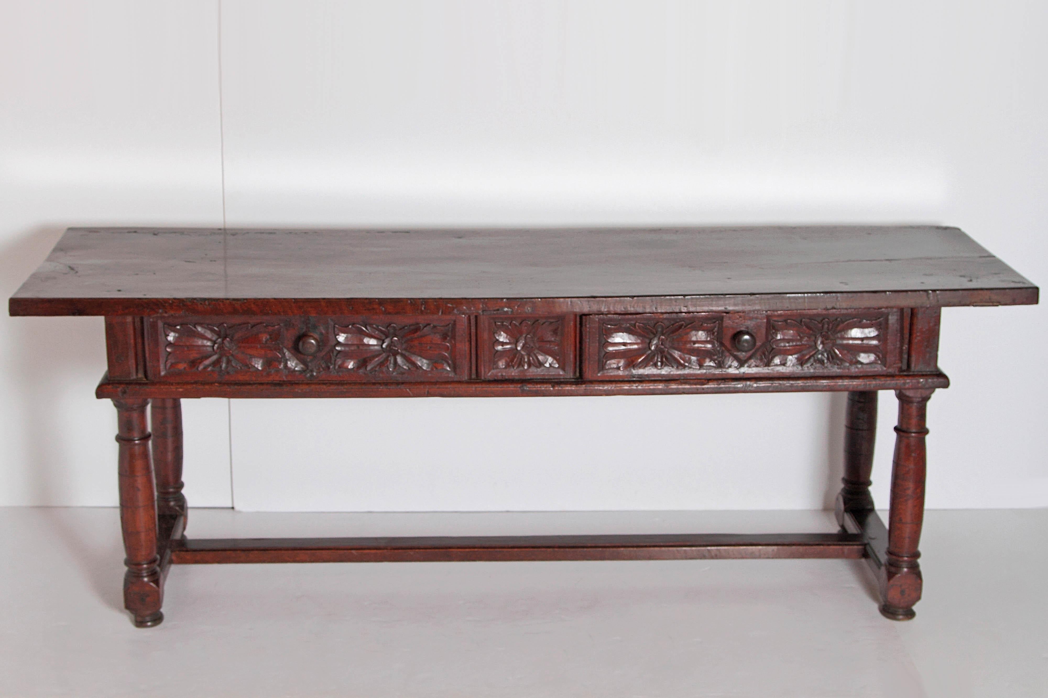 A fine example of a 17th century Spanish hand carved walnut table. A large single board top above two drawers heavily carved with wooden knobs. The sides and back apron are also nicely carved. Beautiful original color and patina. Standing on trestle