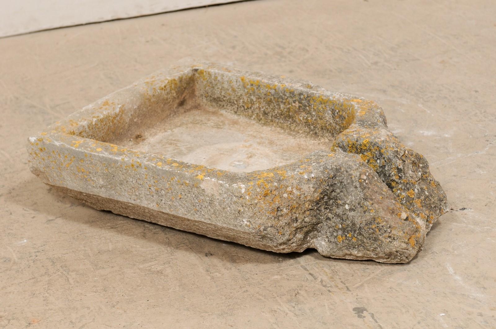 A 19th century Spanish hand carved stone trough. This antique stone trough from Spain, likely once used in the production to press olives into oil, features a mostly-squared body with a projecting spout at one end side. A single drain hole is within