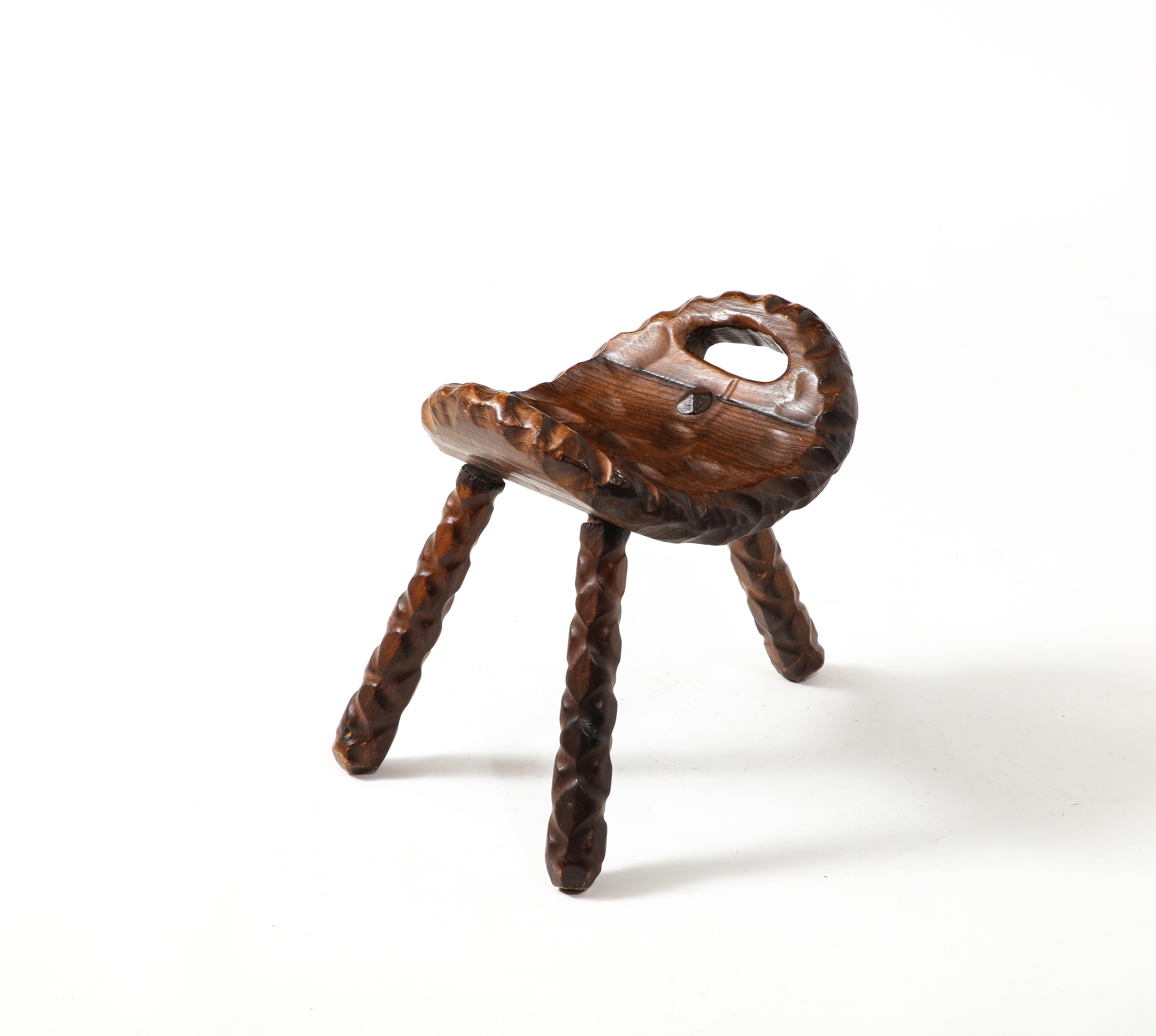 Intricately carved tripod stool with a curved seat. 