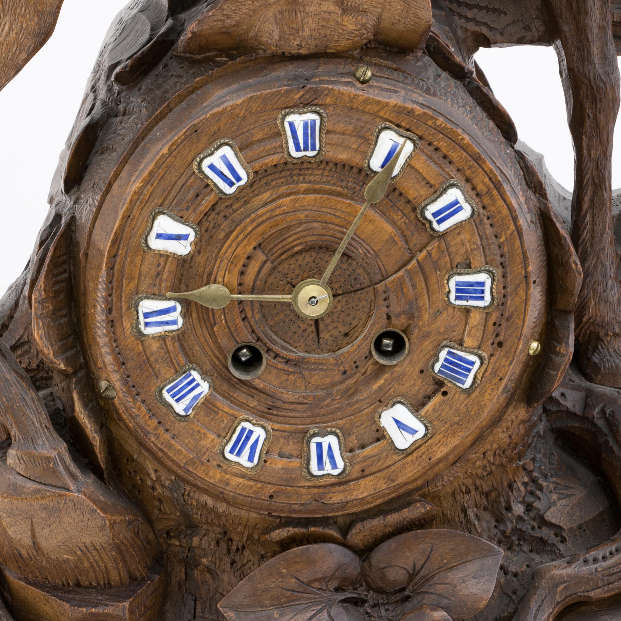 Hand-carved Swiss Black Forest mantle clock. Featuring a large red stag standing on branch and stump natural base with foliage accents, with fence behind. In working condition. Clock face with white roman numerals and brass hands. Circa 1900. 18