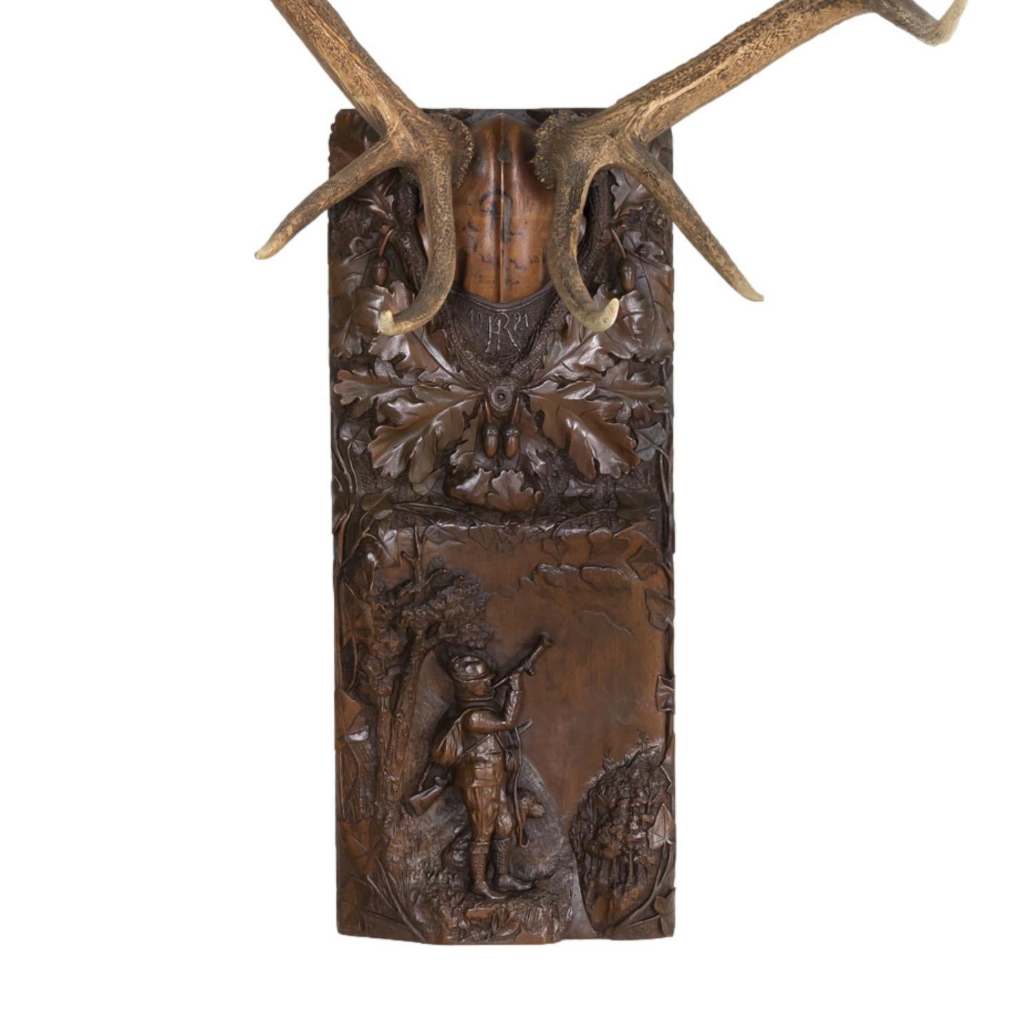 A stunning antique Black Forest carved wooden trophy plaque with a large set of antlers signed and dated 1815 mounted atop a large hand carved plaque featuring a collar or wreath of intricately carved oak leaves and acorns with the initials RH and