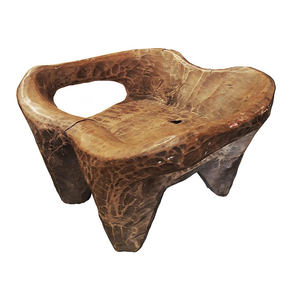An Indonesian hand carved stool from a single piece of distressed teak wood, circa 1960. With four carved legs and curved arms. Use as a low side table or stand. A unique piece that will add an interesting accent to any eclectic decor.