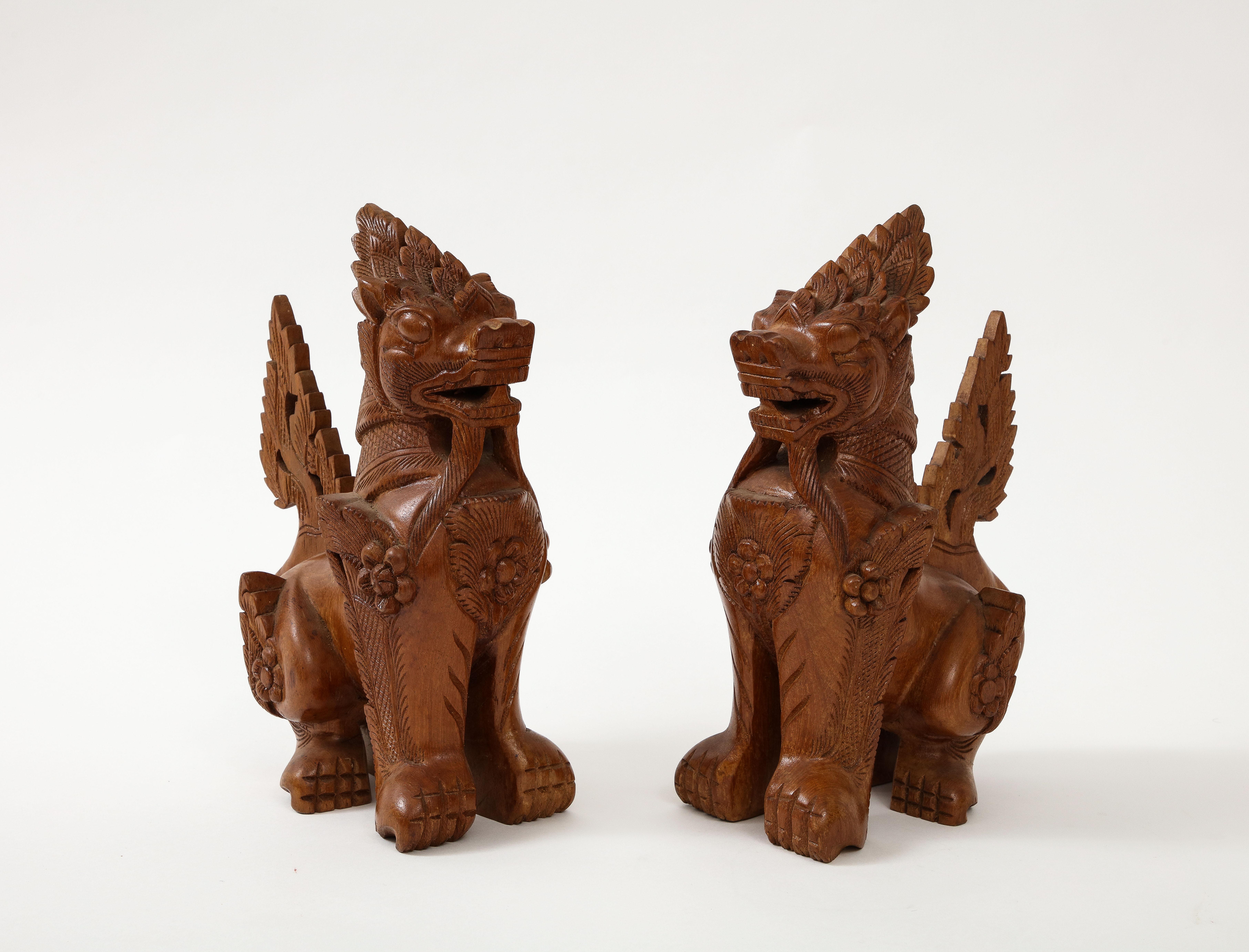 Pair of intricately hand carved Teak temple guard dogs. Foo dogs are symbolic, protective statues, and they are designed in pairs — one is female, the other is male. The female represents yin, and symbolically protects the people dwelling inside the