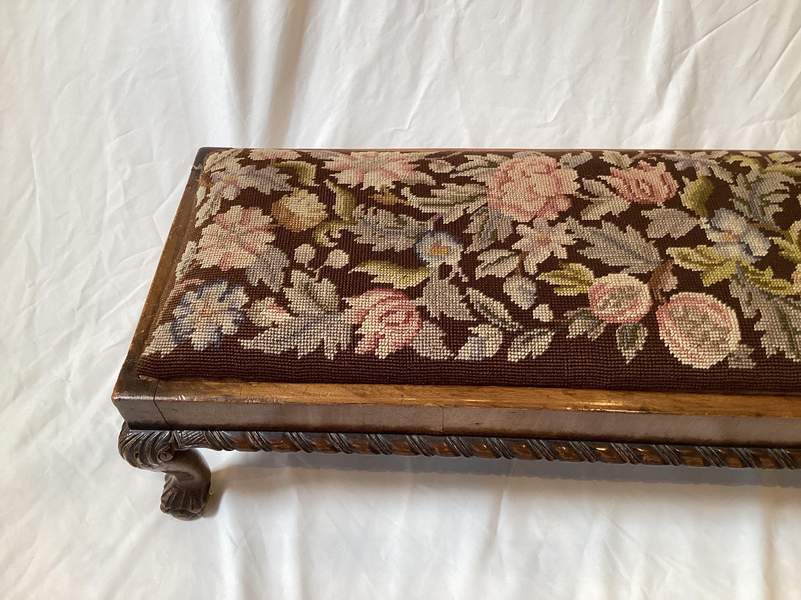 A 19th century hand carved walnut diminutive bench. The carved rope edge with cabriole leg with a hand stitched floral wool needlepoint top. Diminutive size, more of a footrest at 9.5 inches tall, 40 wide, 12 deep.