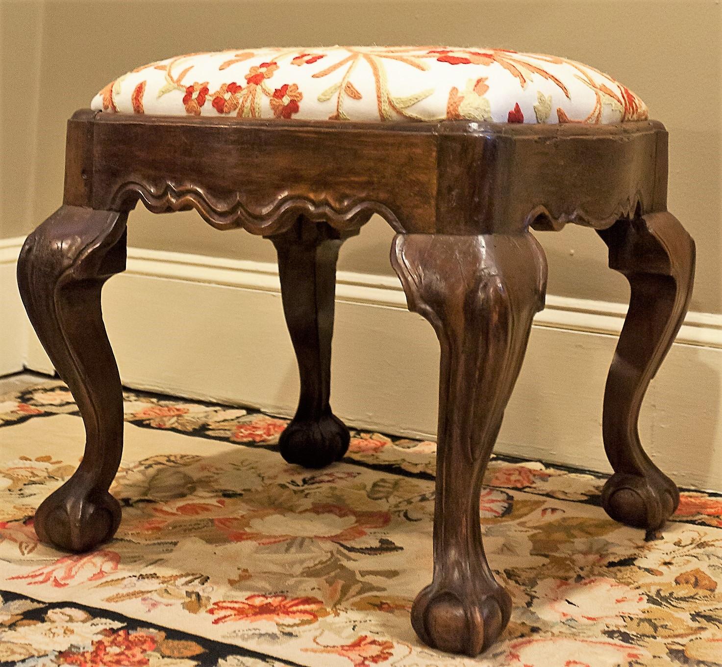 This beautiful Chippendale style walnut stool is hand carved, and the slip seat is upholstered in crewel on an off-white ground. The piece has an old finish and an excellent patina.