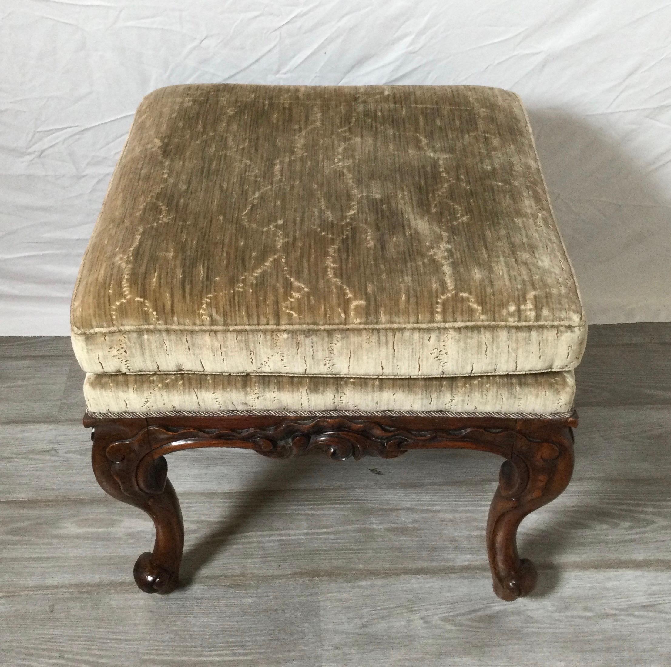 A beautifully hand carve walnut bench with upholstered base and legs with upholstered attached cushion top. The fabric withought tears or stains in a faded dusty gray blue. the graceful cabriole legs in a rich dark walnut color with excellent