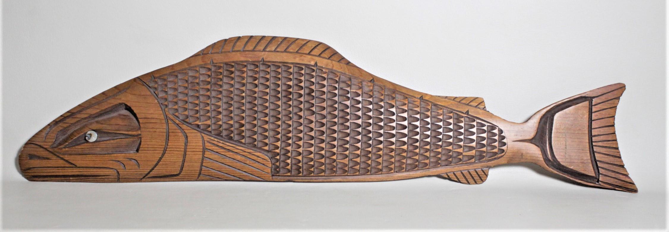 This hand carved Salmon wall sculpture was done by Mei Good in the Haida West Coast British Columbia style in circa 1960. This large carving is quite detailed in the treatment of the stylized scales with deep geometrically shaped cuts and flowing