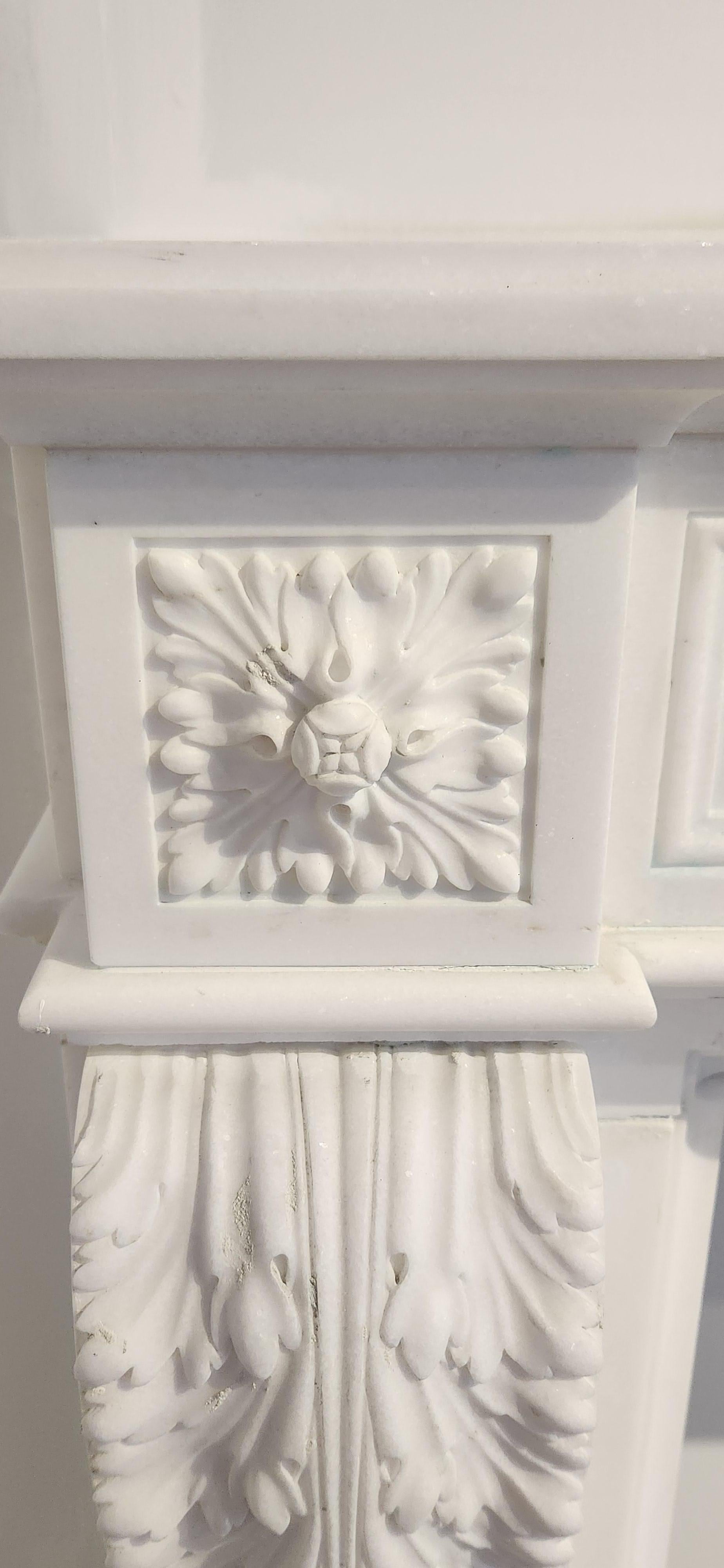 This gorgeous Regency-style fireplace mantel is hand-carved in beautiful white marble. The marble is a bright white, and is very clean, with virtually no veining. The hand-carved details on the fireplace include an intricately-carved wreath and