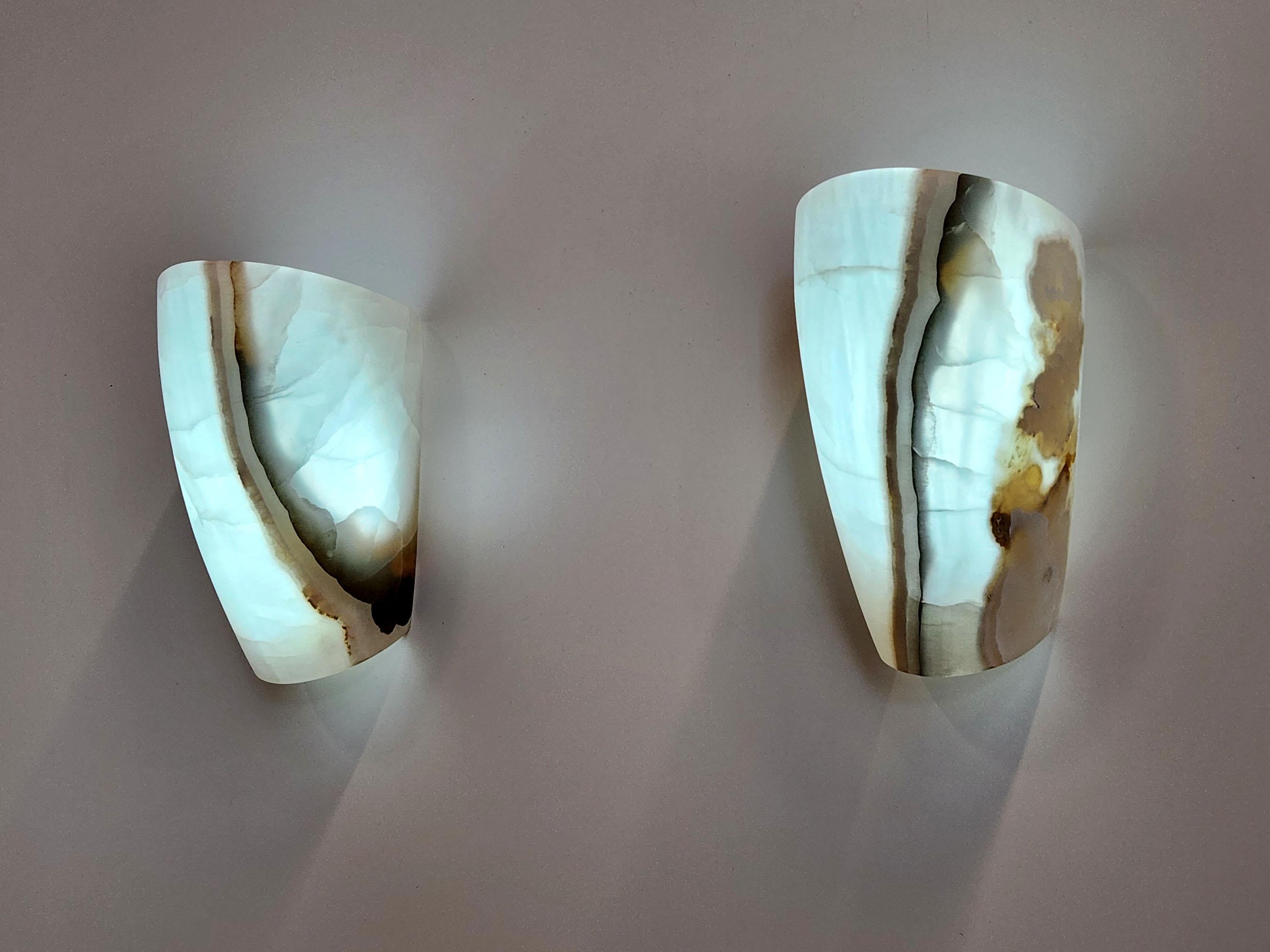 This is an all Onyx ambient sconce, with a high and surprising contrast in luminosity. When lit, the light accentuates the differences in the translucency of the stone. It ranges from the highly translucent white and light brown. 

Although there