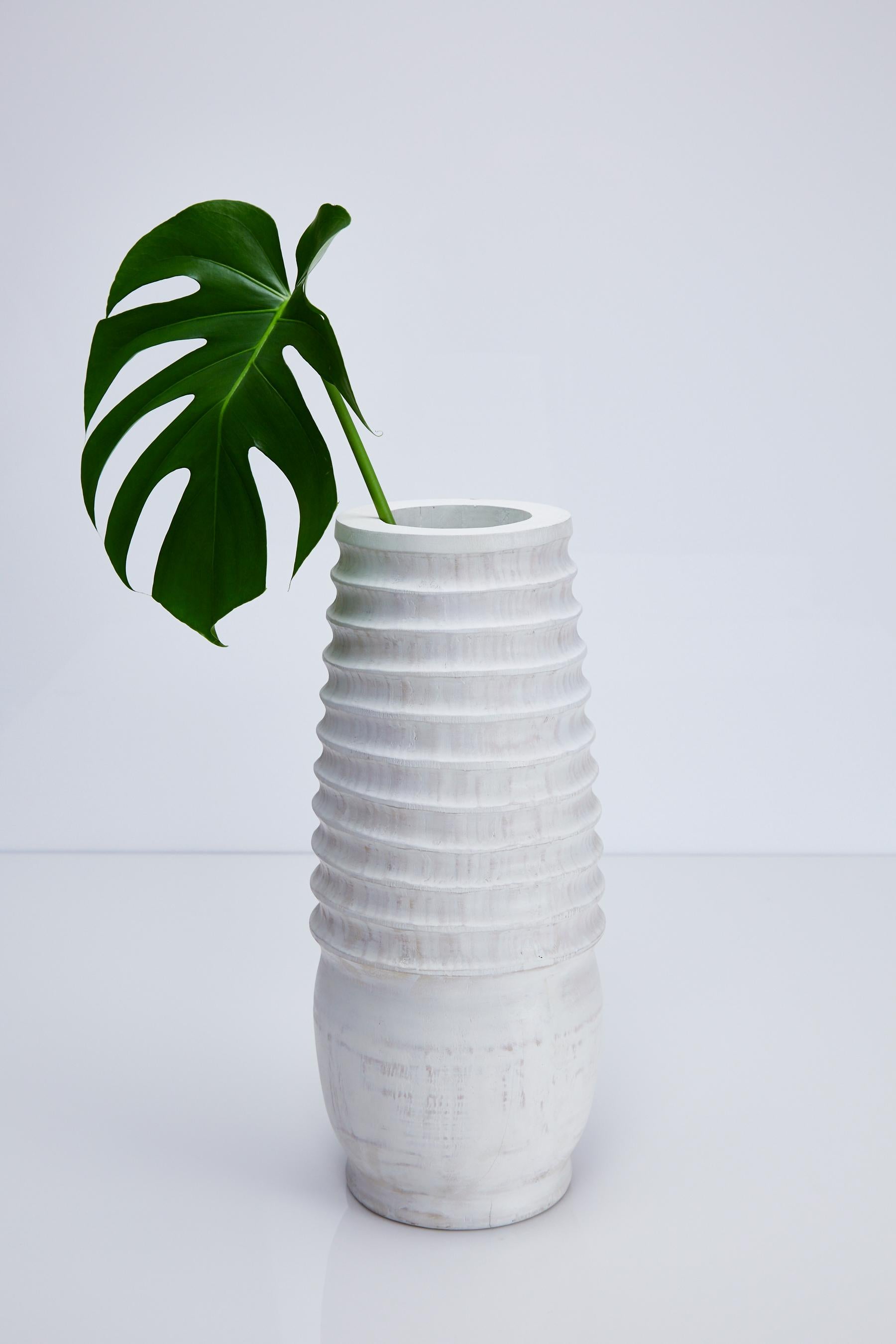 Medium sized hand carved wooden vase with ribbing extending 3/4 of the way down the body. Vase has distressed white-washed finish.