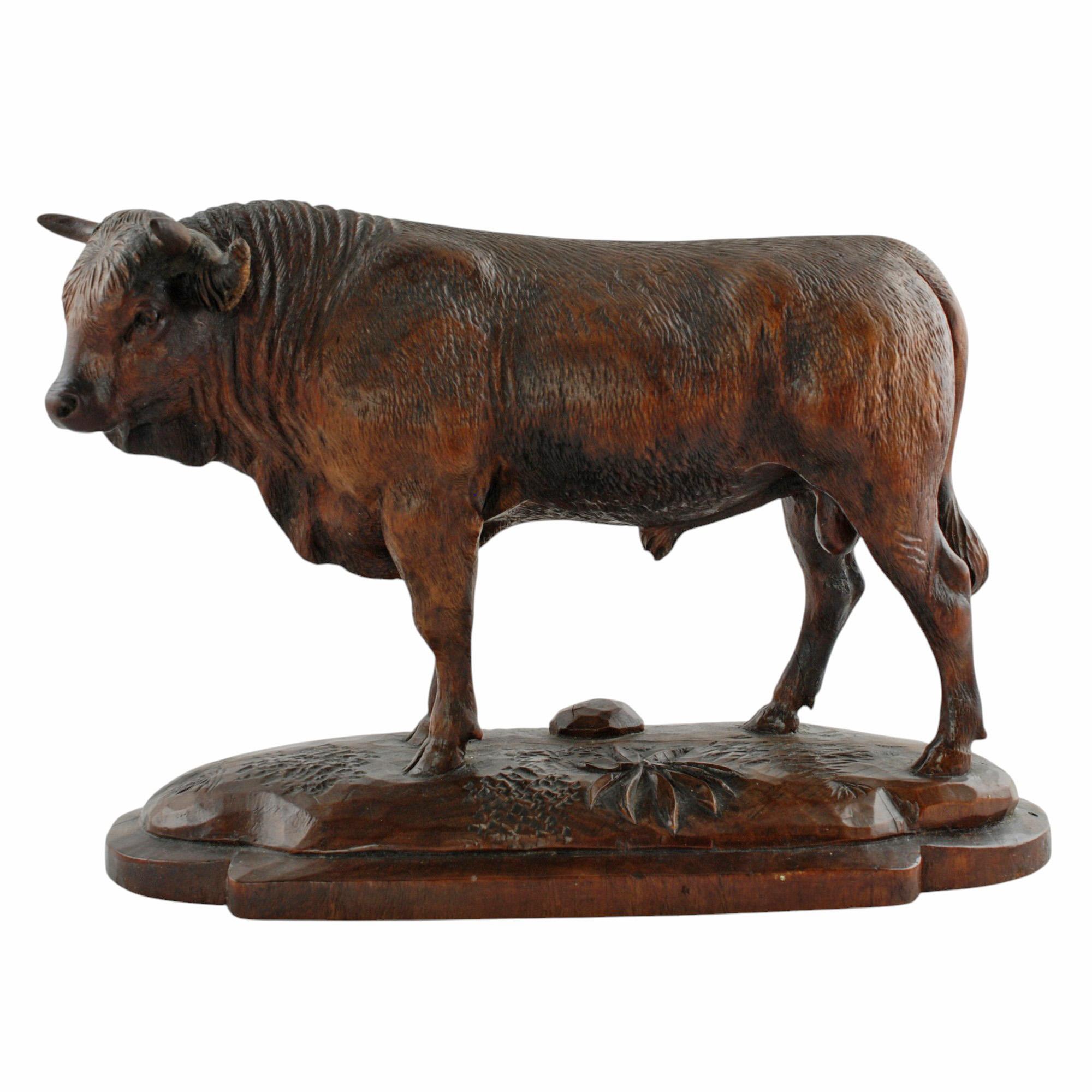 Ce taureau figuratif sculpté à la main et habilement exécuté est entièrement dimensionnel et a une riche couleur brune. Le taureau est représenté en position debout sur un socle en bois façonné. L'animal musclé a été fini avec des détails réalistes,