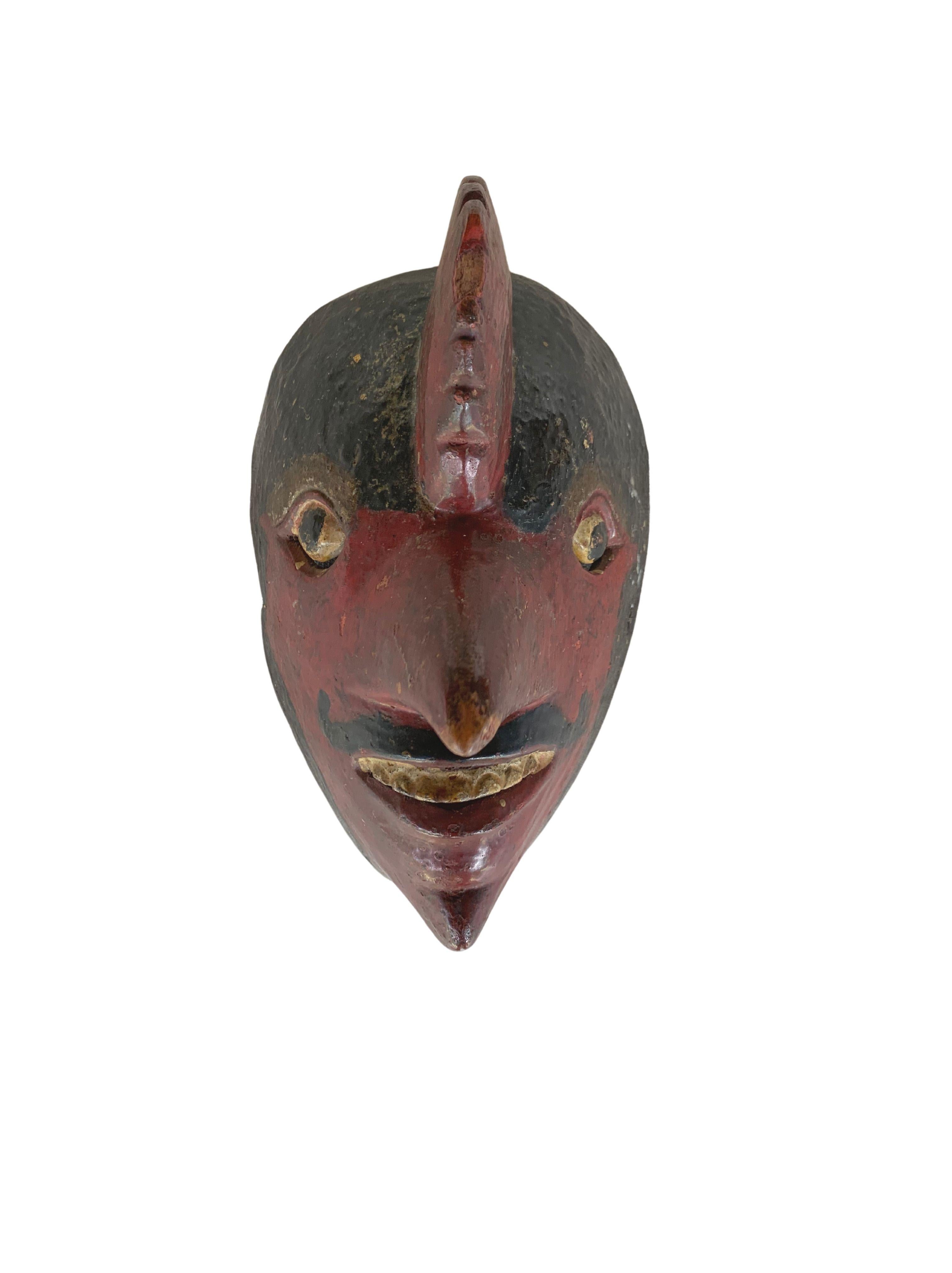 This early 20th century ‘Wayang topeng’ mask was used in Javanese masked dance performances. This mask features a dark red polychrome and resembles a bird-man with an extended and exaggerated nose. It is visibly old with fading of the original
