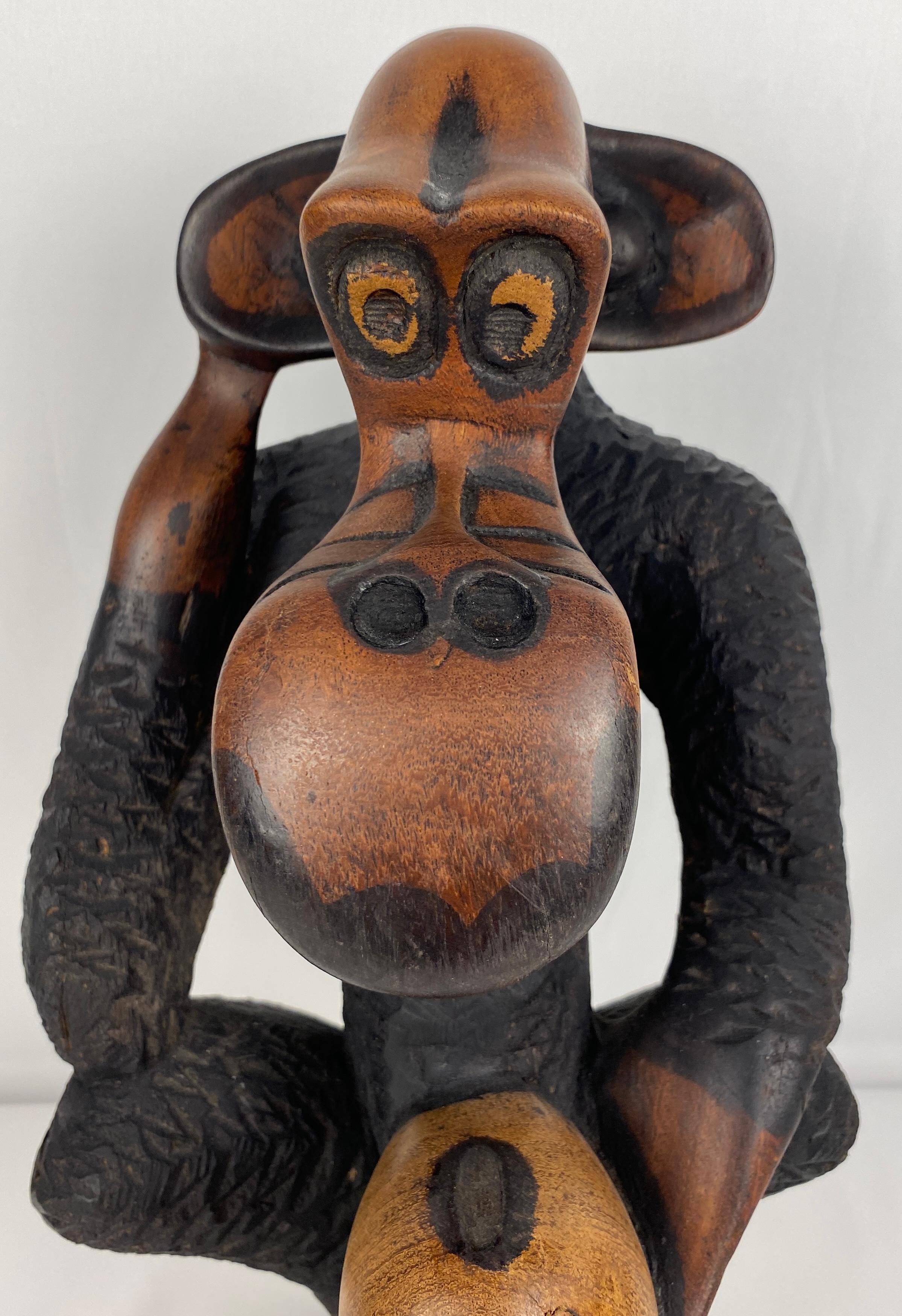 A playful wooden sculpture. 
Seated, holding what appears to be a piece of fruit, this intricately carved monkey is almost life like. 

The piece is signed on the bottom base.
Measures: 15' High x 8