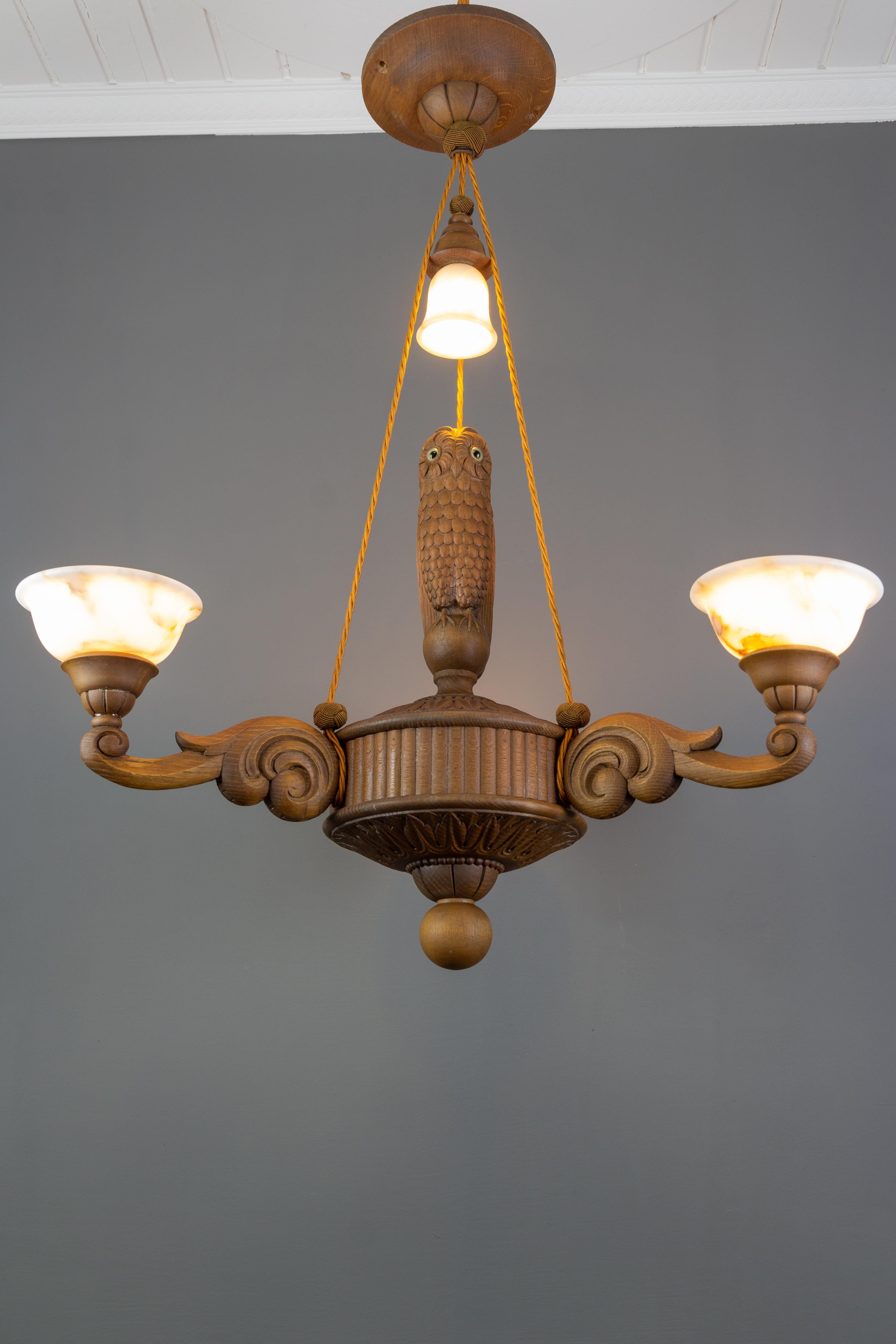 Beautiful and impressive four-light wooden chandelier with an owl figure, Germany, the 1930s. The hand carved chandelier features three arms, each with an alabaster lampshade and an adorable wooden figure of an owl in the center of the chandelier,