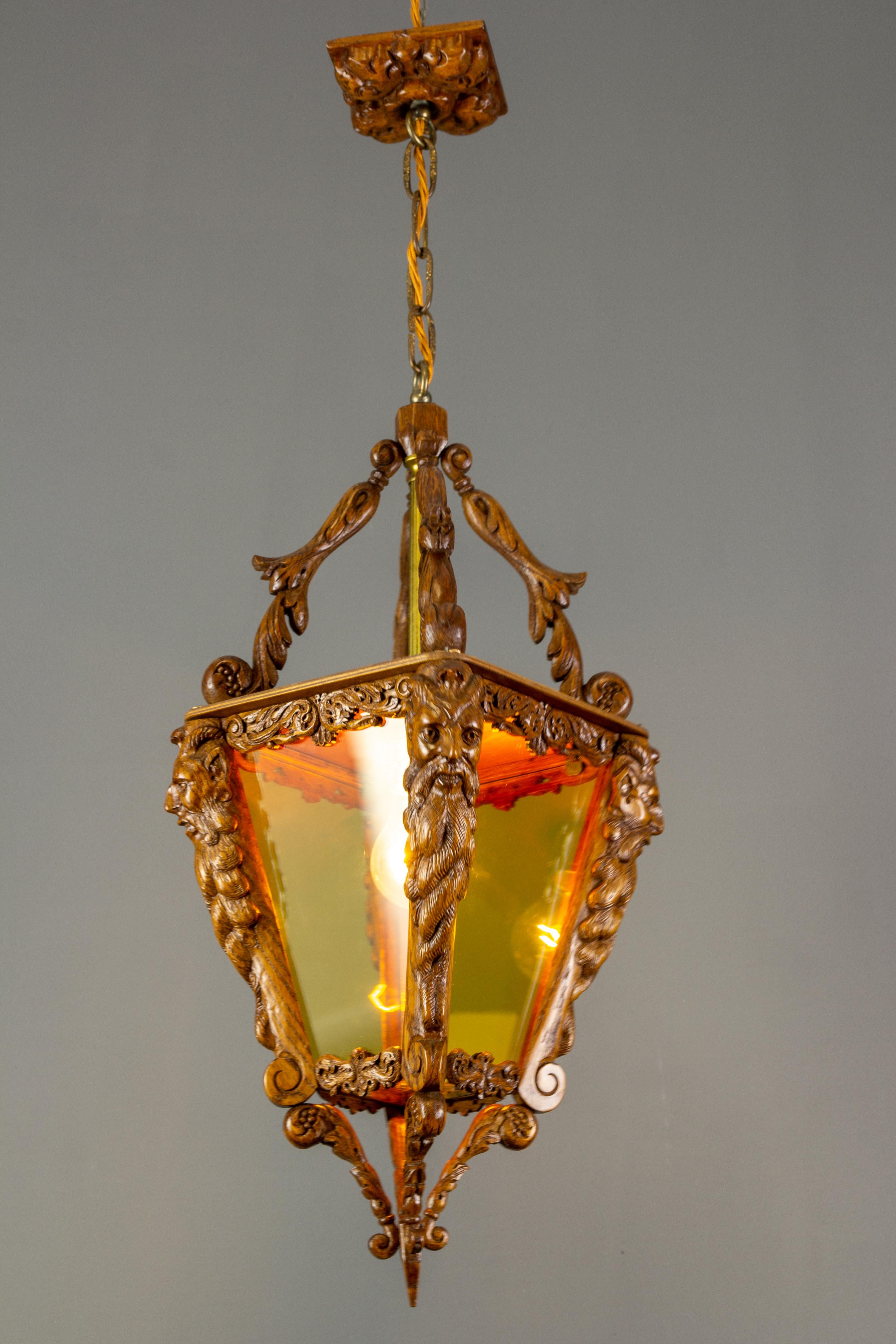 A beautiful and finely hand-carved wooden lantern with yellow glass, Belgium, circa the 1960s. Masterful carved wooden details such as acanthus leaves and four Bacchus heads on each corner of the lantern feature exceptional carving workmanship. Even