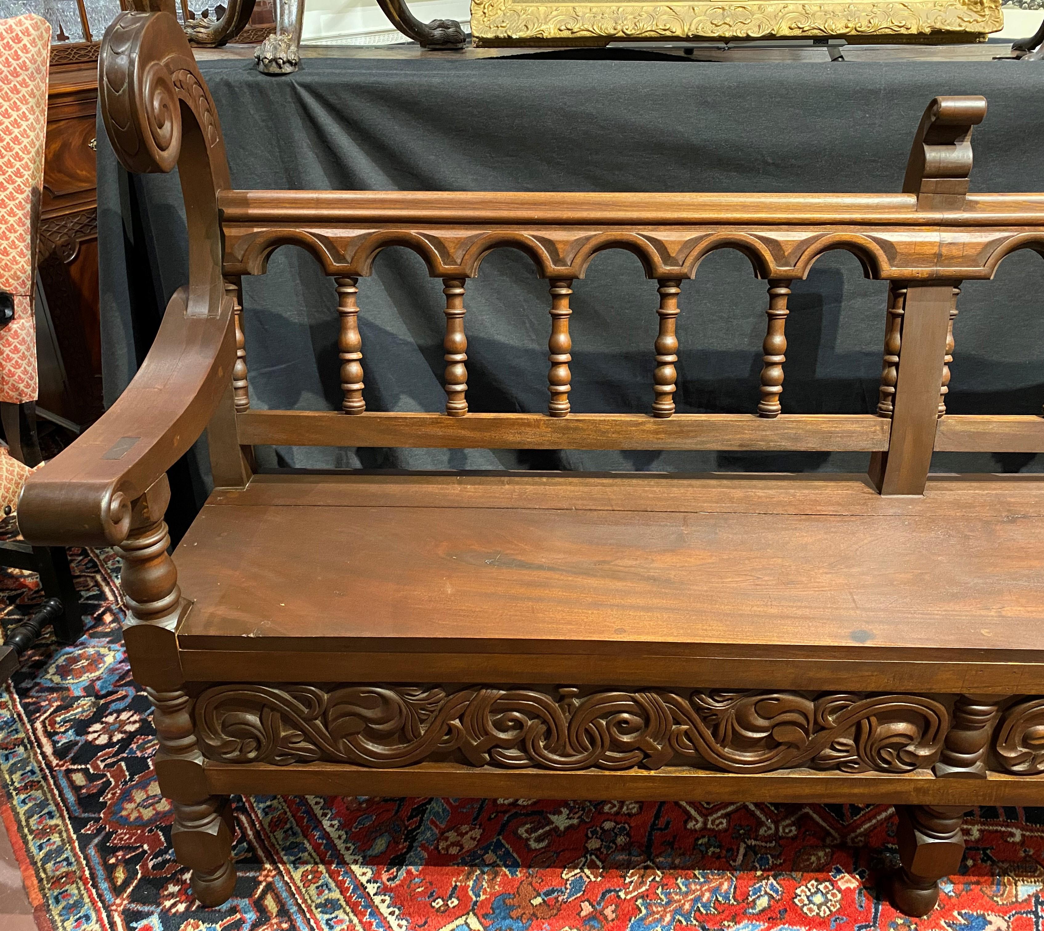 A beautifully detailed two thirds scale copy of an 18th century hand carved church pew from La Merced Cathedral in Antigua, Guatemala with scroll carved crest ends, arms, front panels, and side shield coat of arms panels, turned spindle backs, and