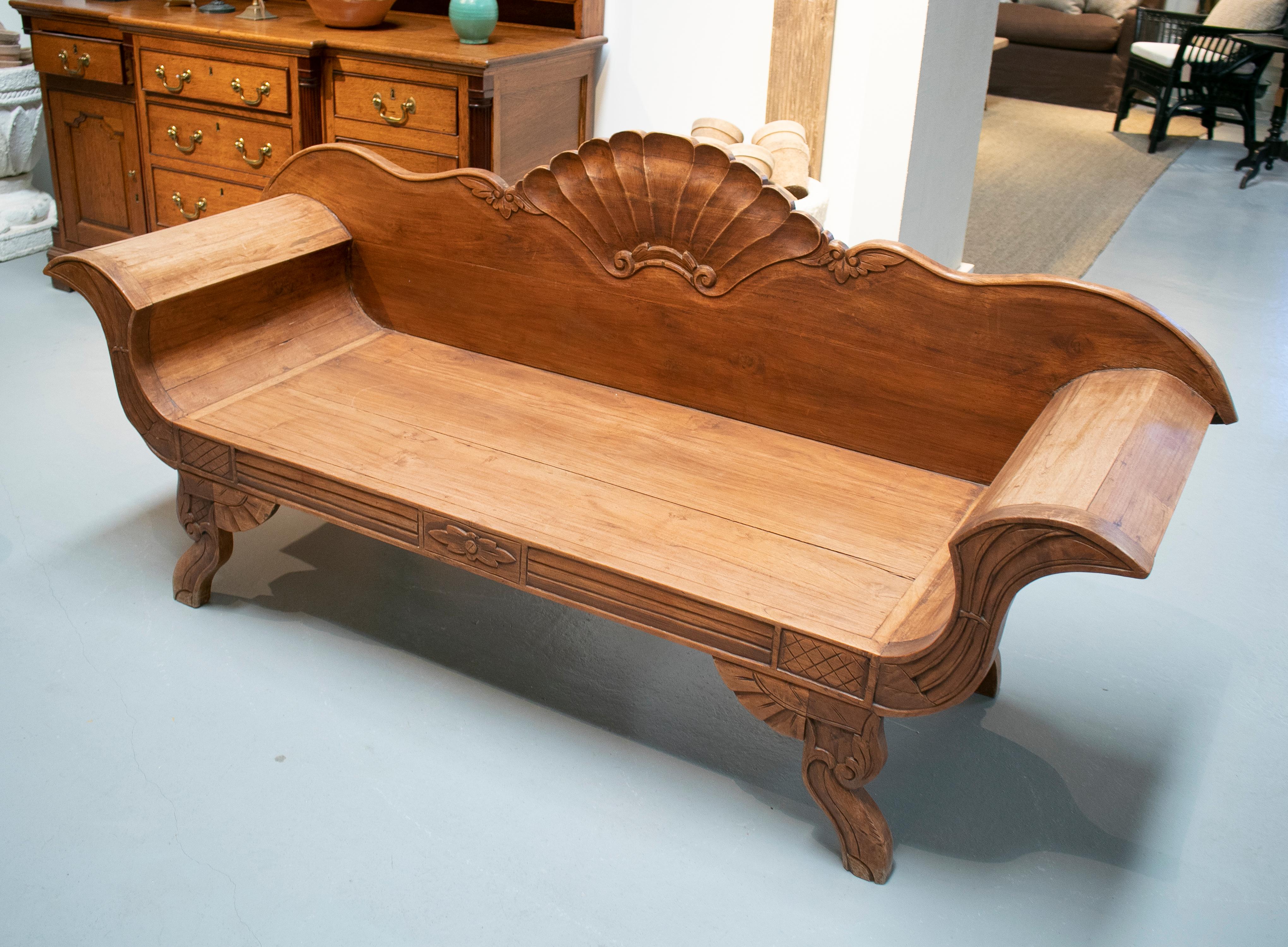 Hand carved wooden garden bench with conch shaped crown decoration and armrests.