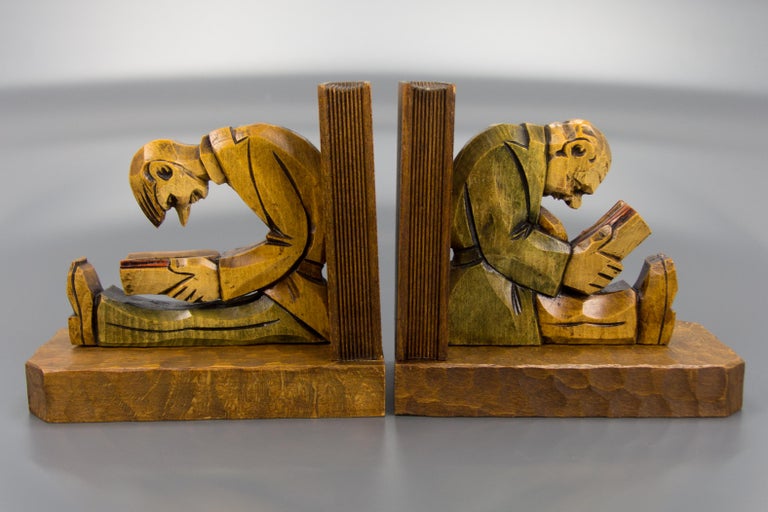 These beautifully hand carved wooden bookends feature sculptures of two sitting and reading man, an older and younger man that could be a teacher and a student. Both sit leaning on supports that are carved in the form of books. Slightly toned in