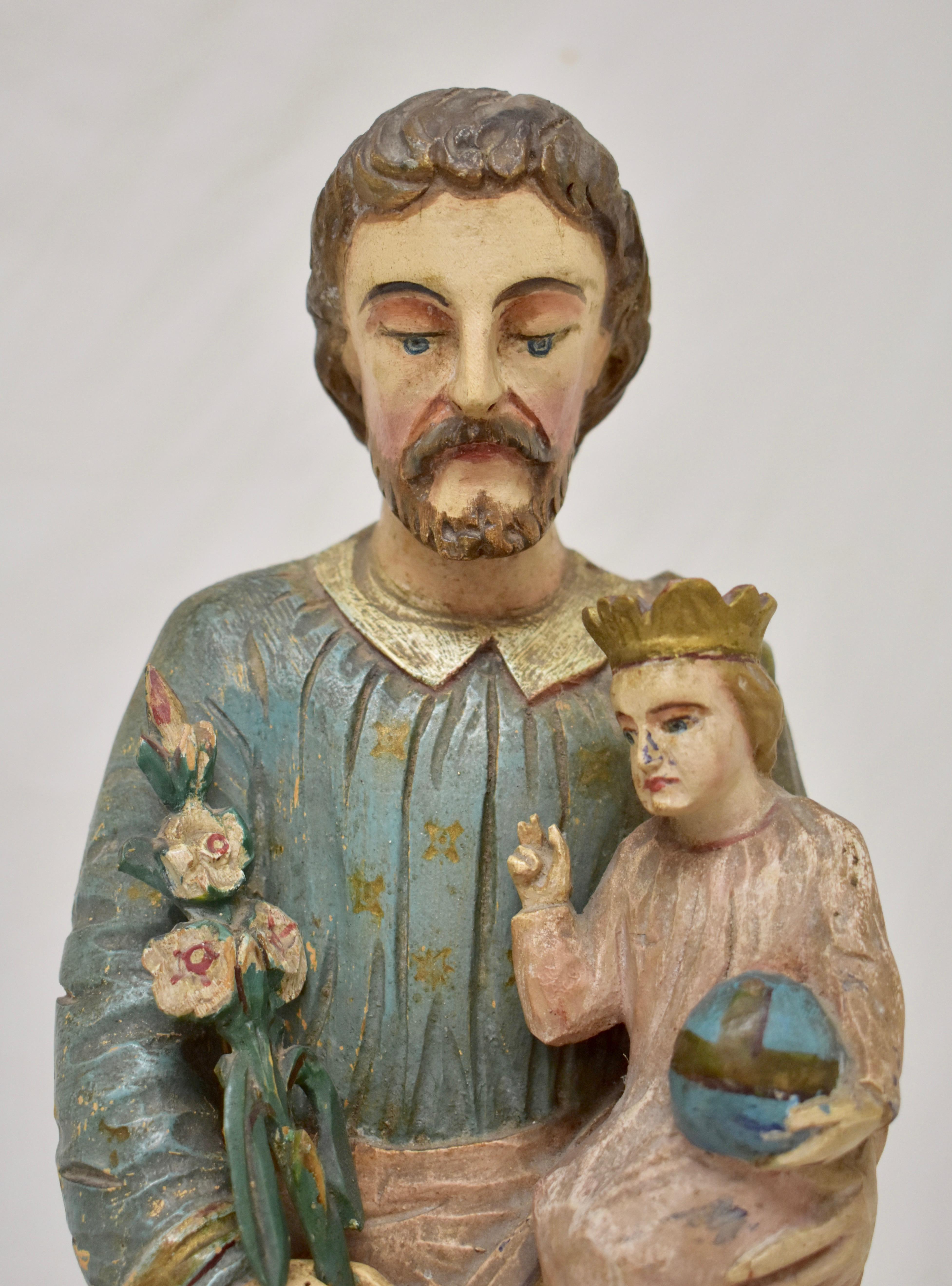 This is a striking Primitive hand carved statue of Saint Joseph.  The Saint stands with head slightly bowed and with a reverent expression. He is clothed in a long blue tunic bearing pressed, gold-painted floral buds, beneath a green toga, slung