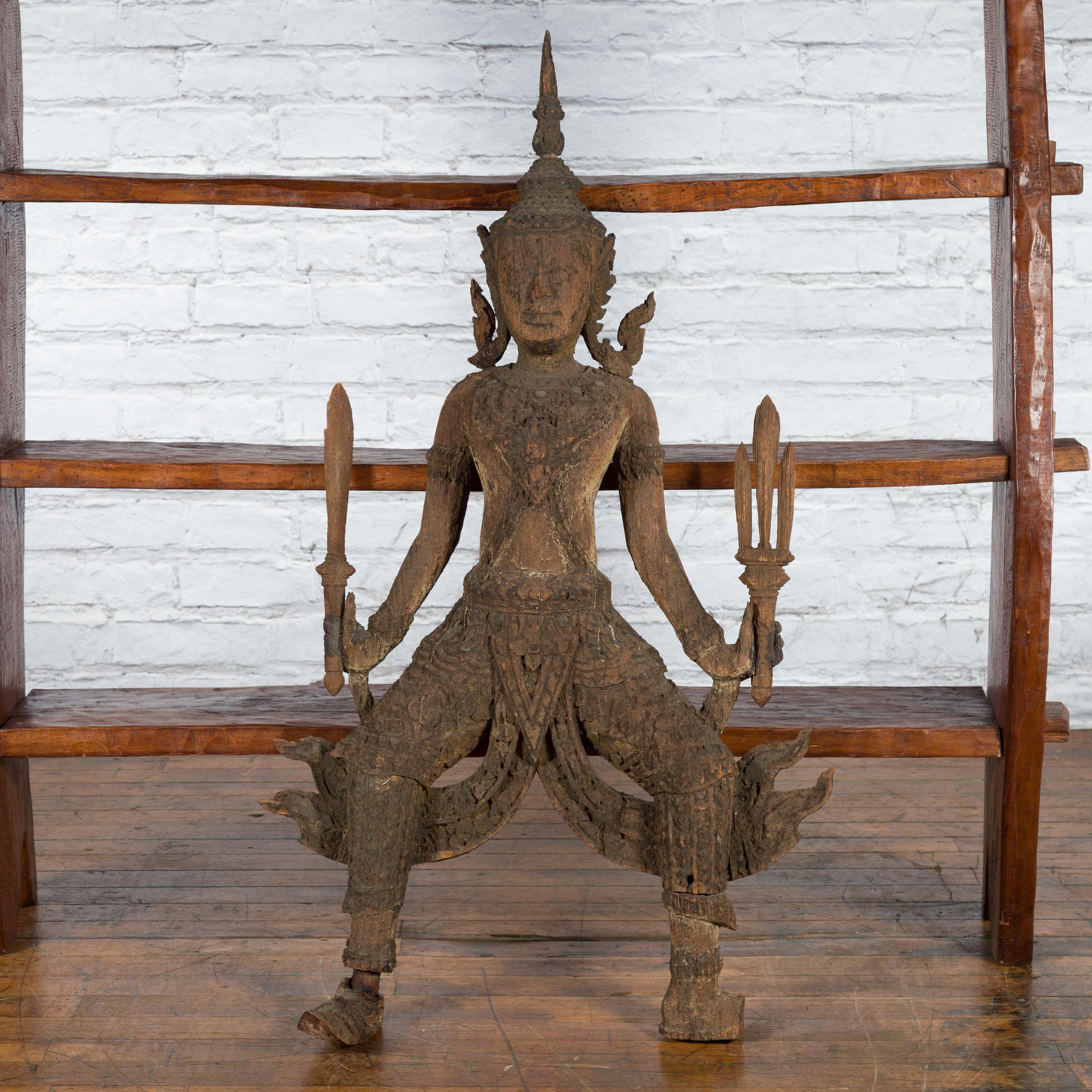 A large hand-carved temple sculpture from the 19th century depicting a Thai warrior holding a sword and a trident, with great distressed appearance. Created in Thailand, this four-foot tall wooden sculpture depicts a Thai warrior ready for battle.