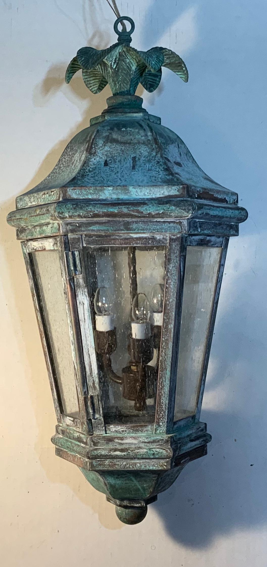 Funky lantern made of handcrafted solid brass, bronze top with decorative palm leaf motif, weathered patina, electrified with three 40/watt lights, good for wet locations and would look great indoor as chandelier. Seeded glass.