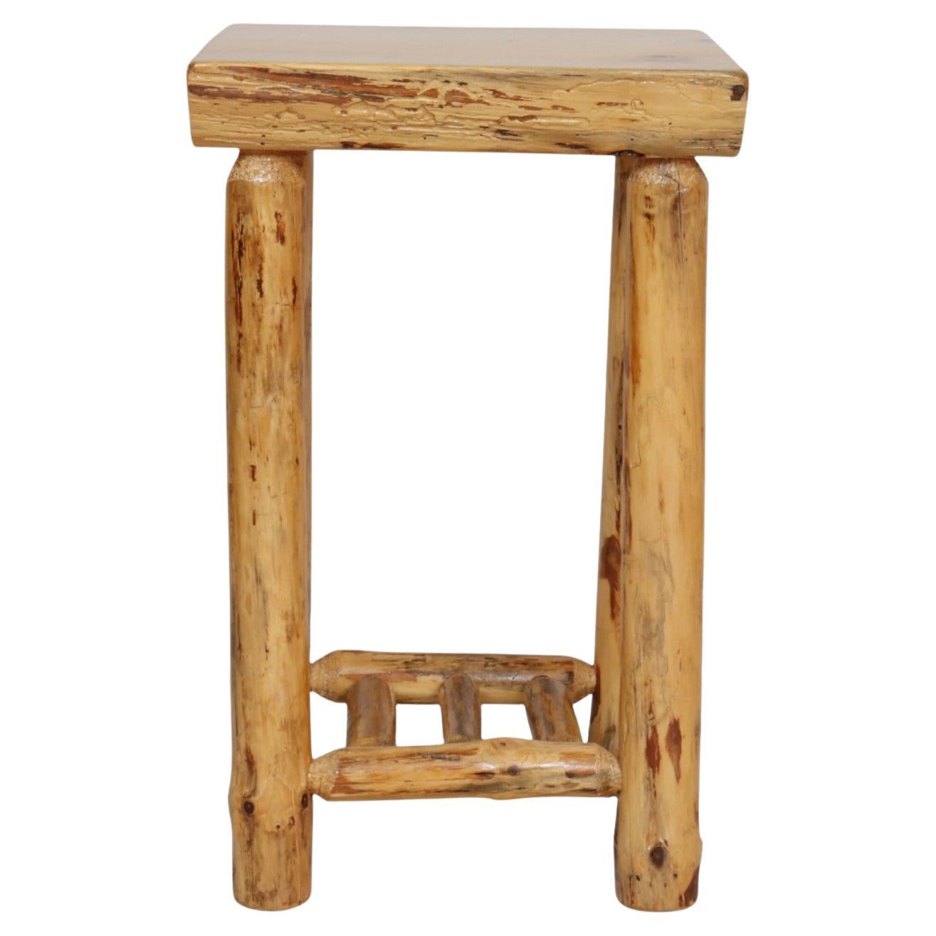 Un tavolino o un supporto per piante in legno lavorato a mano. Il piano quasi quadrato poggia su gambe scrostate a mano, sostenute da una barella a scaletta.