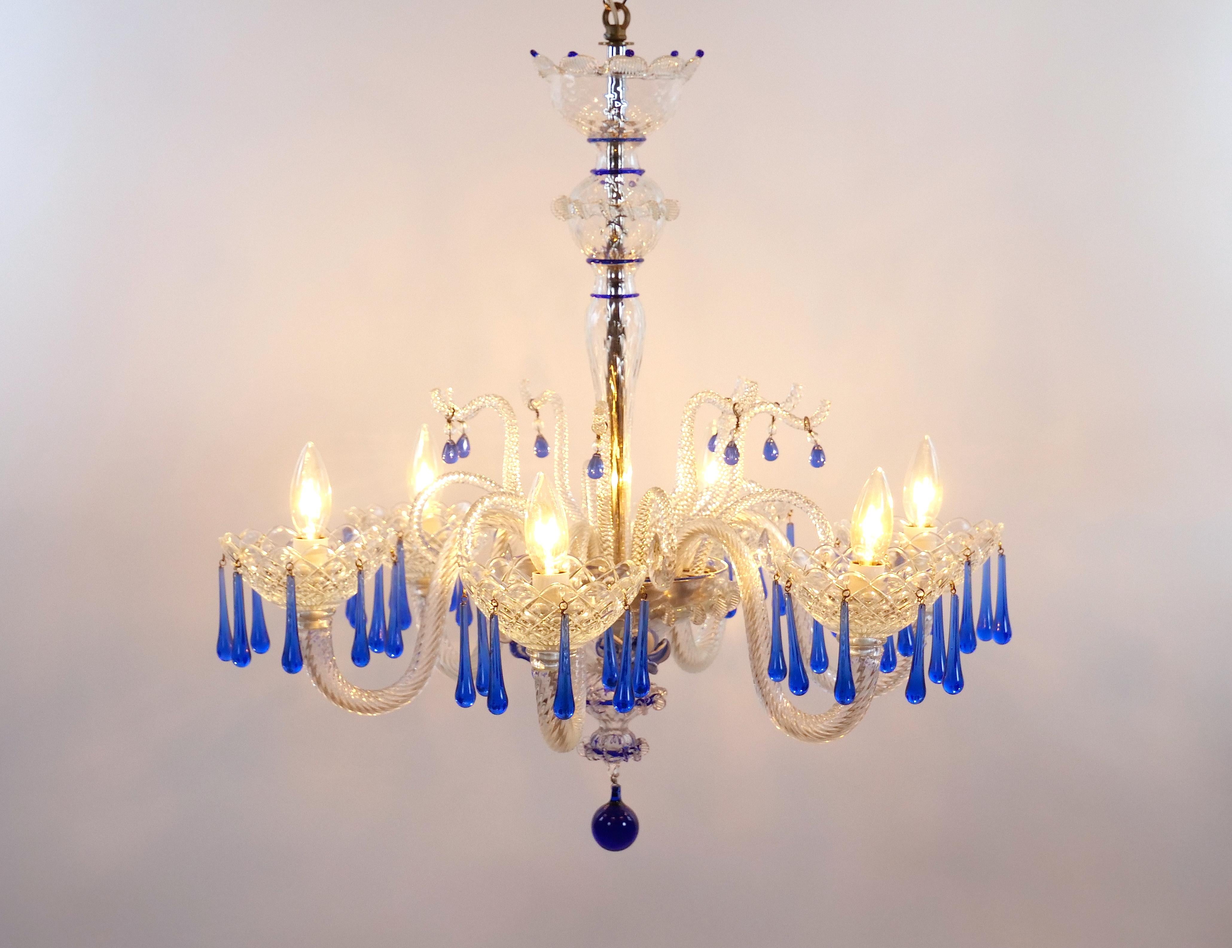 
Indulge in the timeless beauty of this vintage Venetian Italian Murano glass chandelier, a true testament to craftsmanship and elegance. The clear glass standard is adorned with a breathtaking array of blue and white flower heads, each intricately