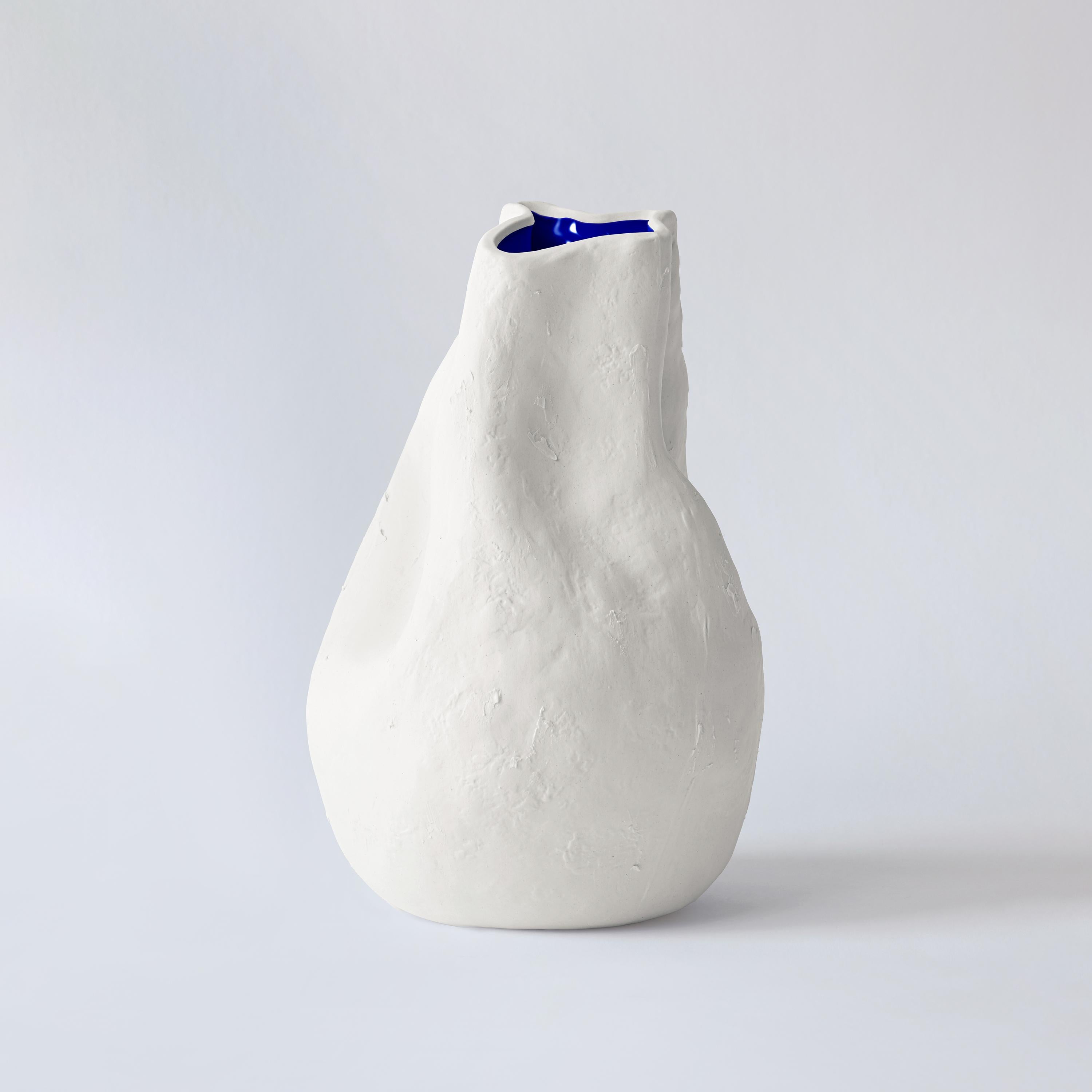 This porcelain hand-crafted vase from The Vibrant Touch Collection features a unique, tactile surface with a textured unglazed finish that invites touch. The design is characterized by a fluid, organic form that culminates in an elegantly irregular