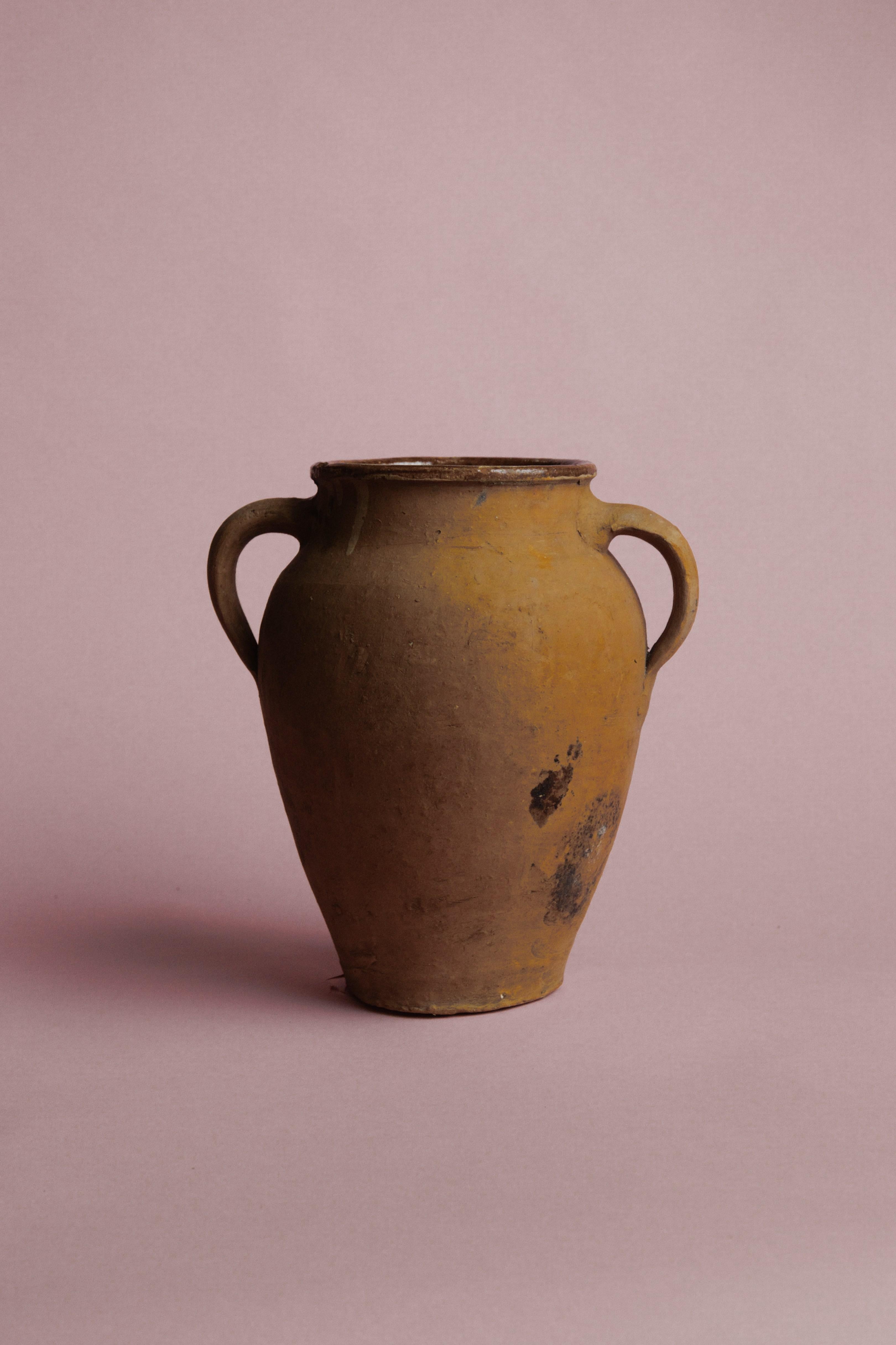 Aggiungi un tocco di charme d'altri tempi al tuo spazio con questo vaso vintage turco a doppio manico in terracotta, uno splendido esempio di artigianato mediterraneo. Realizzato a mano con tecniche tradizionali, questo recipiente rustico in argilla
