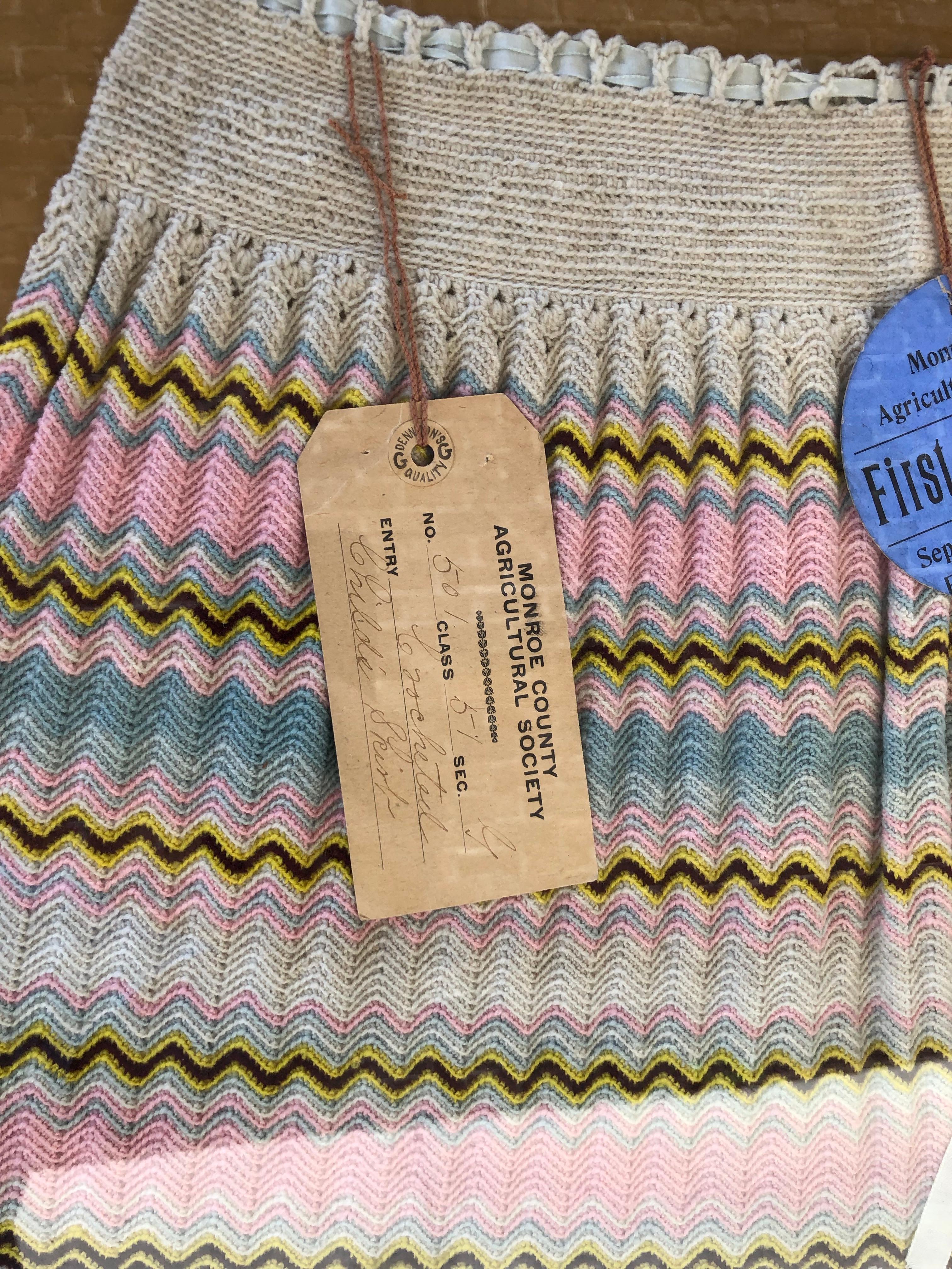 Ein handgehäkelter Kinderrock, der 1908 bei der Landwirtschaftsgesellschaft in Monroe, North Carolina, ausgestellt wurde. Das Baumwollgarn wird zu einem Zickzackmuster in den Farben Creme, Blau, Rosa, Weiß, Gelb und Braun gehäkelt. Das Taillenband