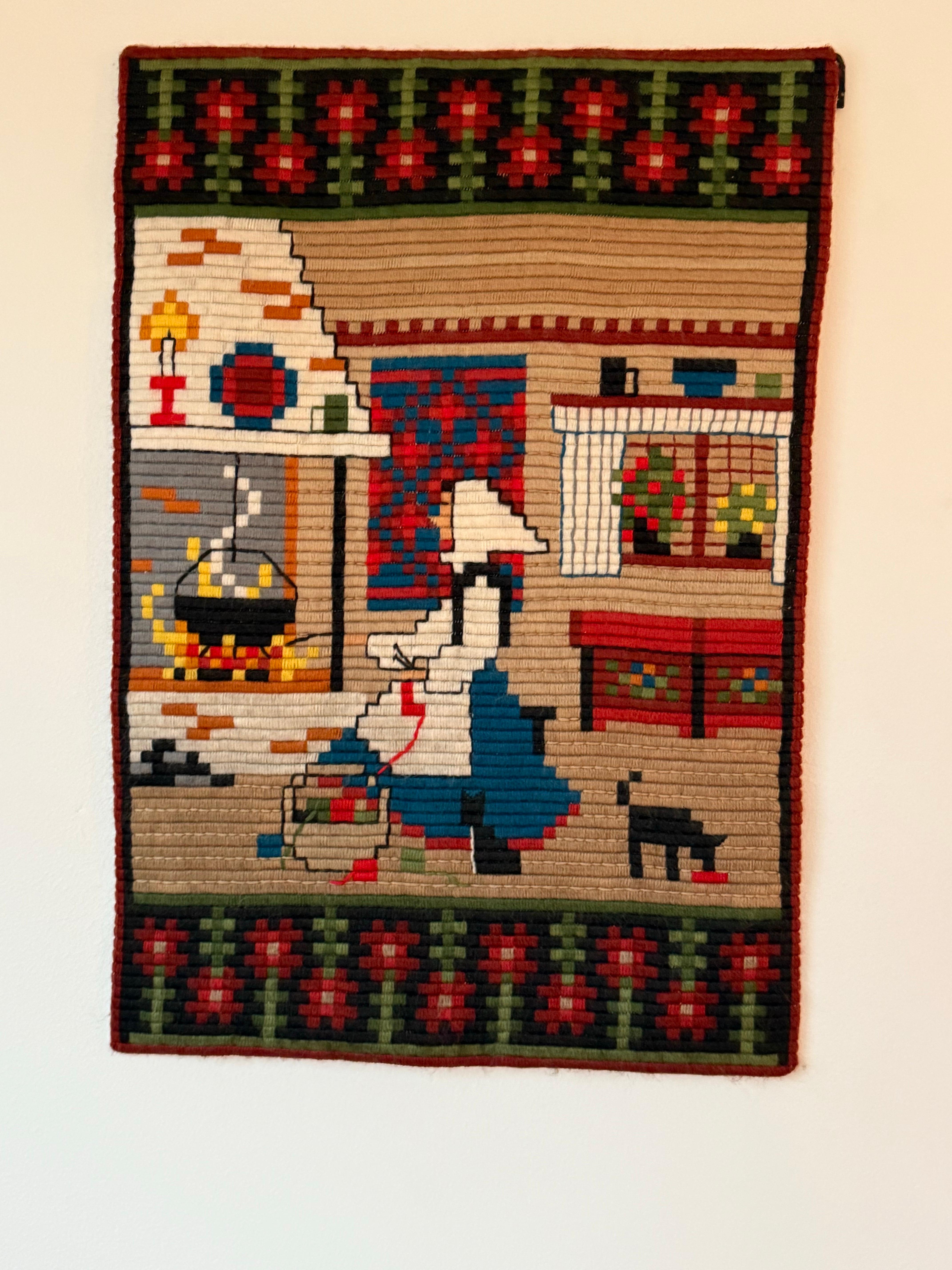 This beautiful hand-embroidered Norwegian tapestry features a charming traditional scene, depicting a woman in folk attire by the fireplace in a cozy, rustic home. With exquisite craftsmanship and intricate details, this piece reflects Norwegian