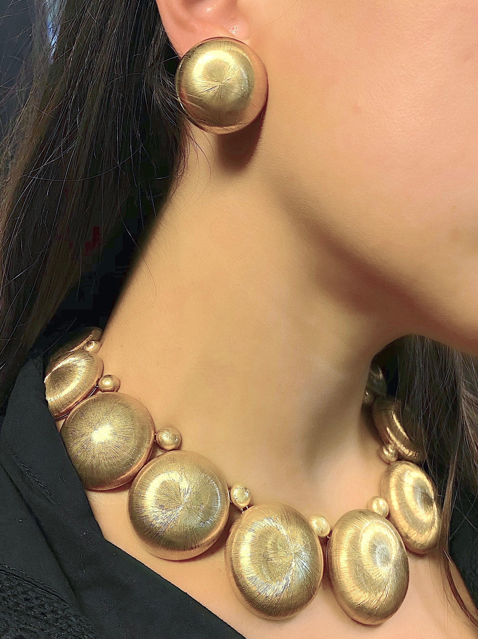 We offer a stunning fashion necklace and ear clip set of graduated and softly rounded 18K gold disks with a unique hand finish simulating thousands of lustrous gold silk threads. A total weigh of 253.8 grams. The necklace disks graduate from 3/4