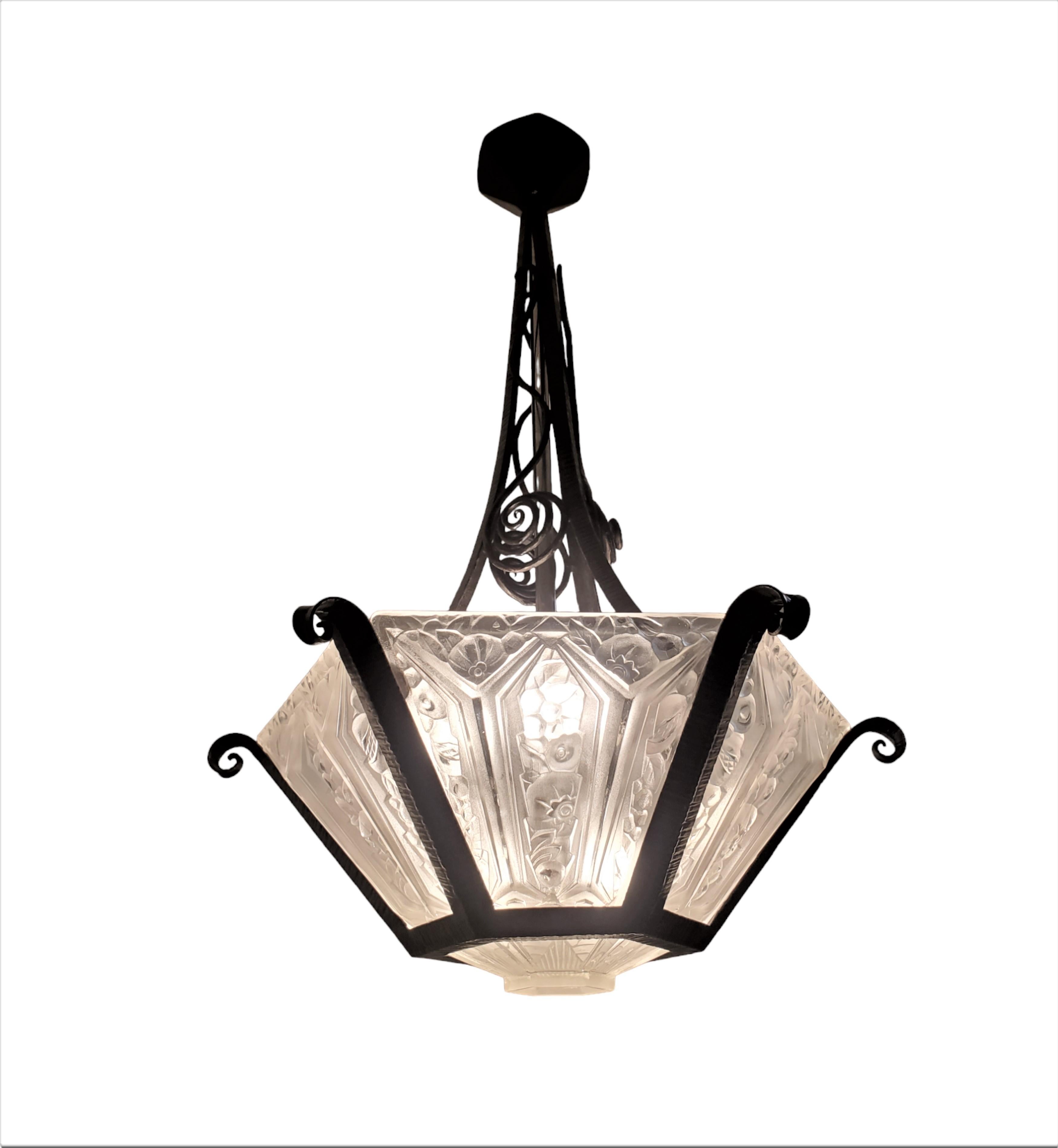 An exquisite French Art Deco chandelier by Verrerie Des Hanots characterized by its trapezoidal-shaped panels arranged in a captivating architectural form, is skillfully crafted within a hand-forged iron original armature. The six frosted art glass
