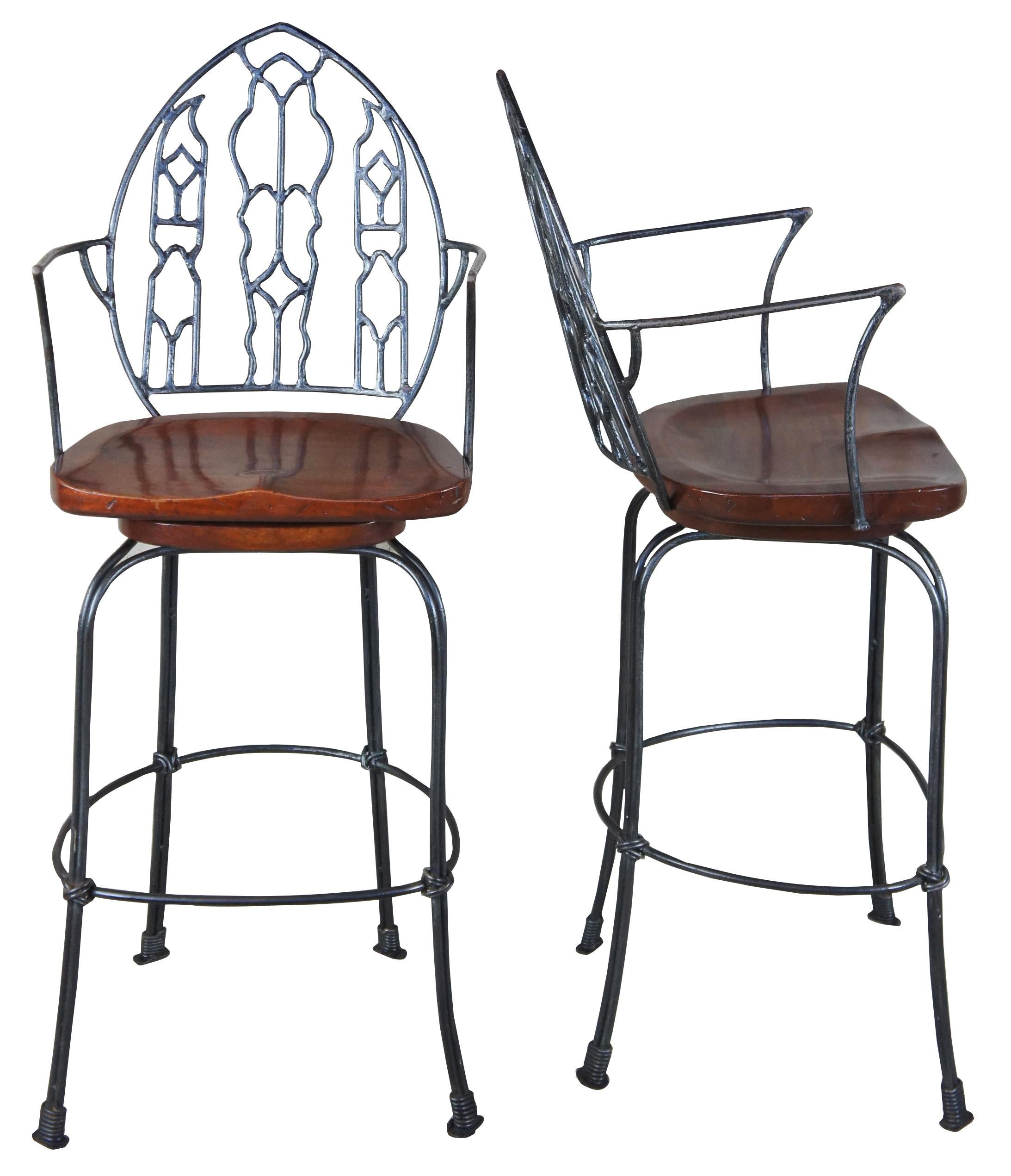 Late 20th century gothic and Spanish inspired wrought iron bar stools with mahogany saddle seat. Stools features swivel action and foot bar. Very heavy.
 