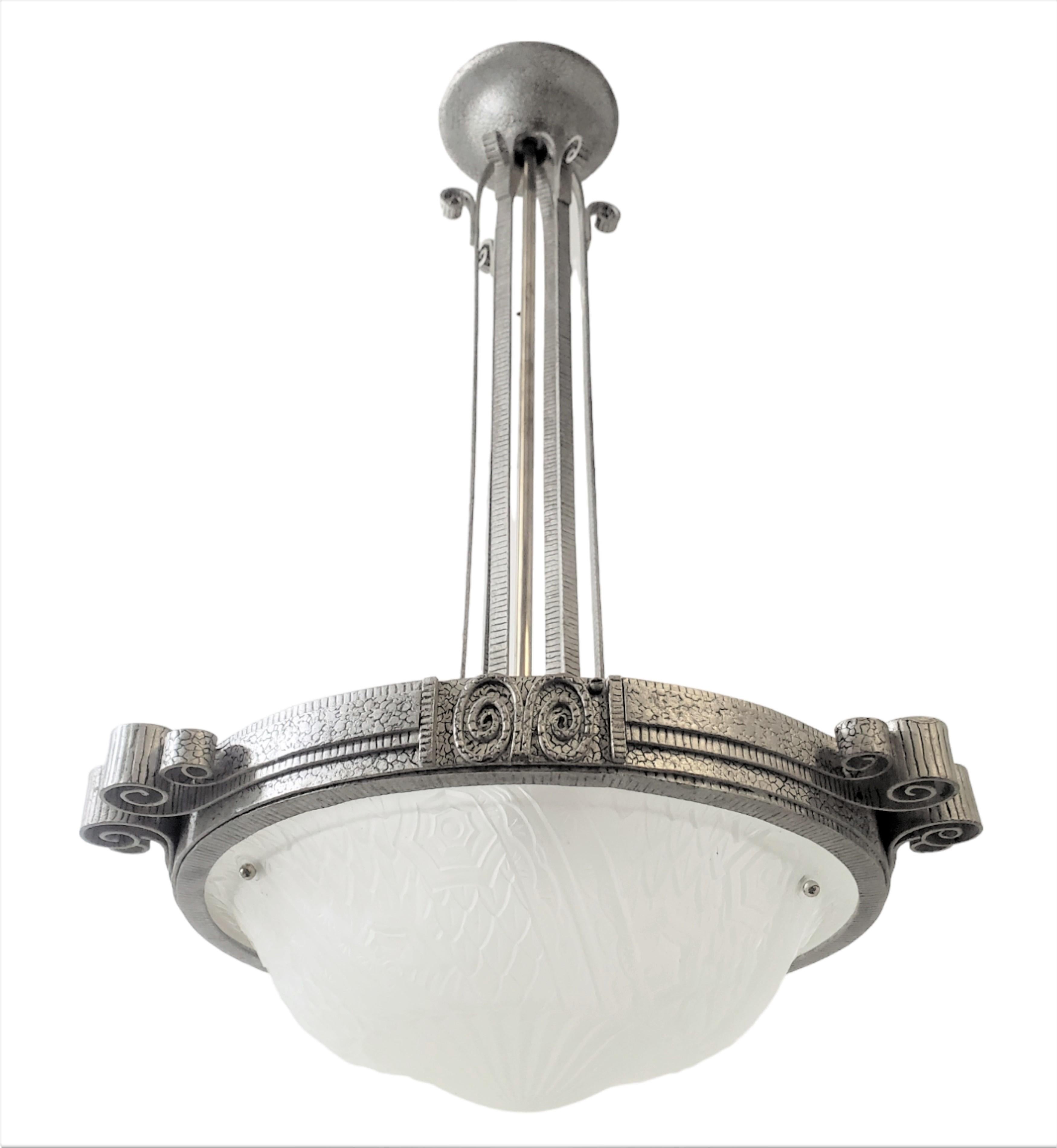 A French Art Deco chandelier, influenced by the Arts and Crafts style, features hand-hammered iron craftsmanship and a sizable frosted glass geometric central coupe. The broad hammered iron surround is adorned with three evenly spaced protruding