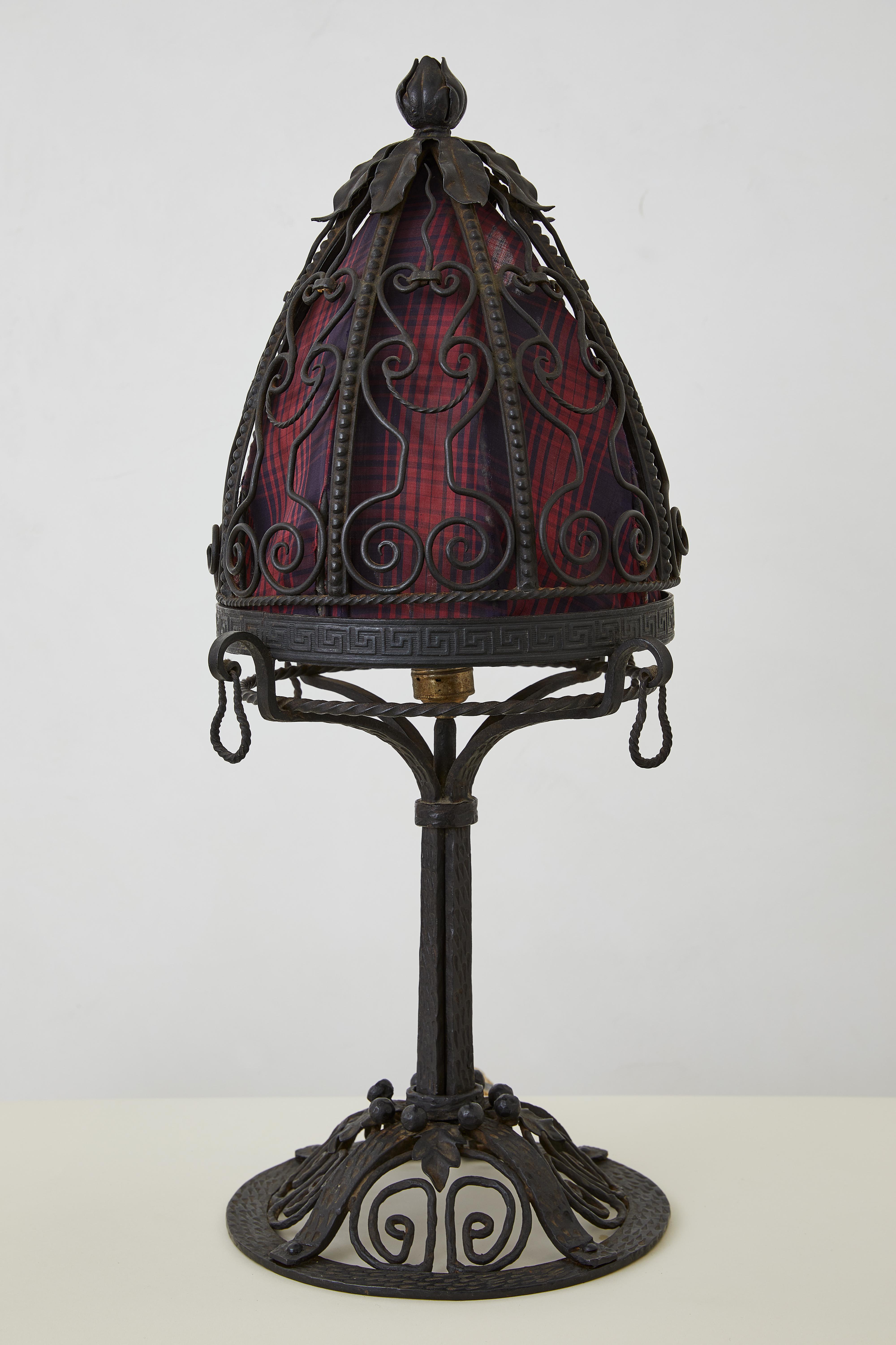 An exquisite hand-hammered Art Deco table lamp, reflecting the intricate detailing and organic forms of early 20th-century European craftsmanship. The sculptural wrought-iron base, adorned with delicate floral motifs, supports a richly patterned