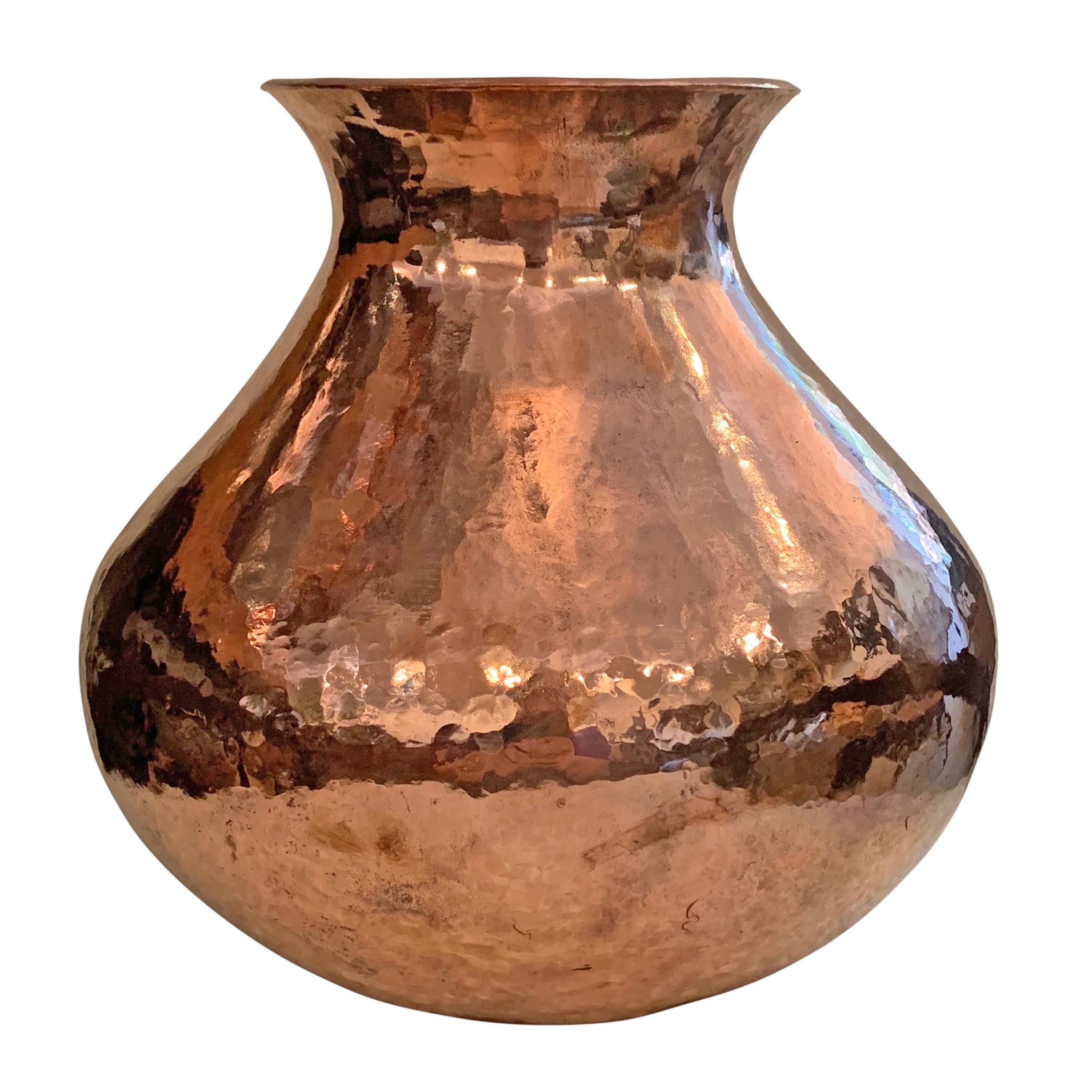A beautiful Mexican hand-hammered copper vase with a wide lip, narrow neck, and a full belly. Perfect for holding flowers or for display on a shelf or table.