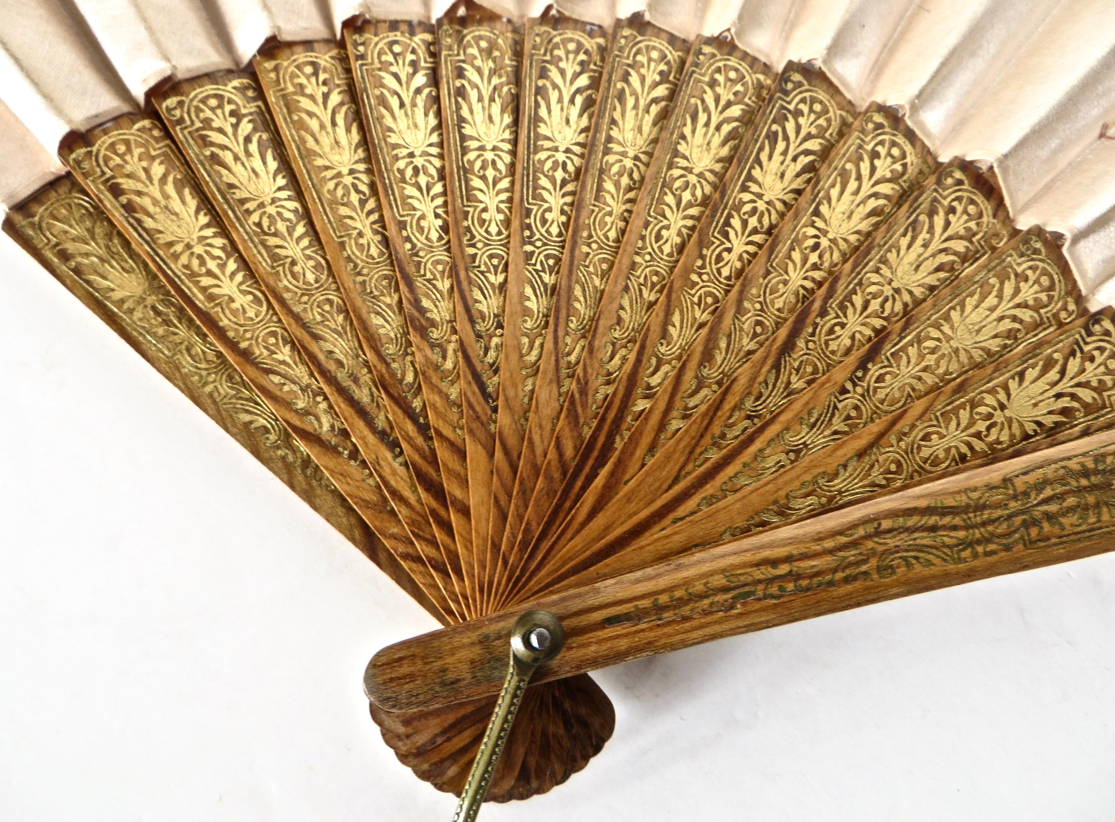 Hand held 19th century fan, circa 1880 is of European manufacture; probably French, and has seven hand painted floral bouquet designs in pretty colors of blue and gold, on champagne colored fabric. The top 3