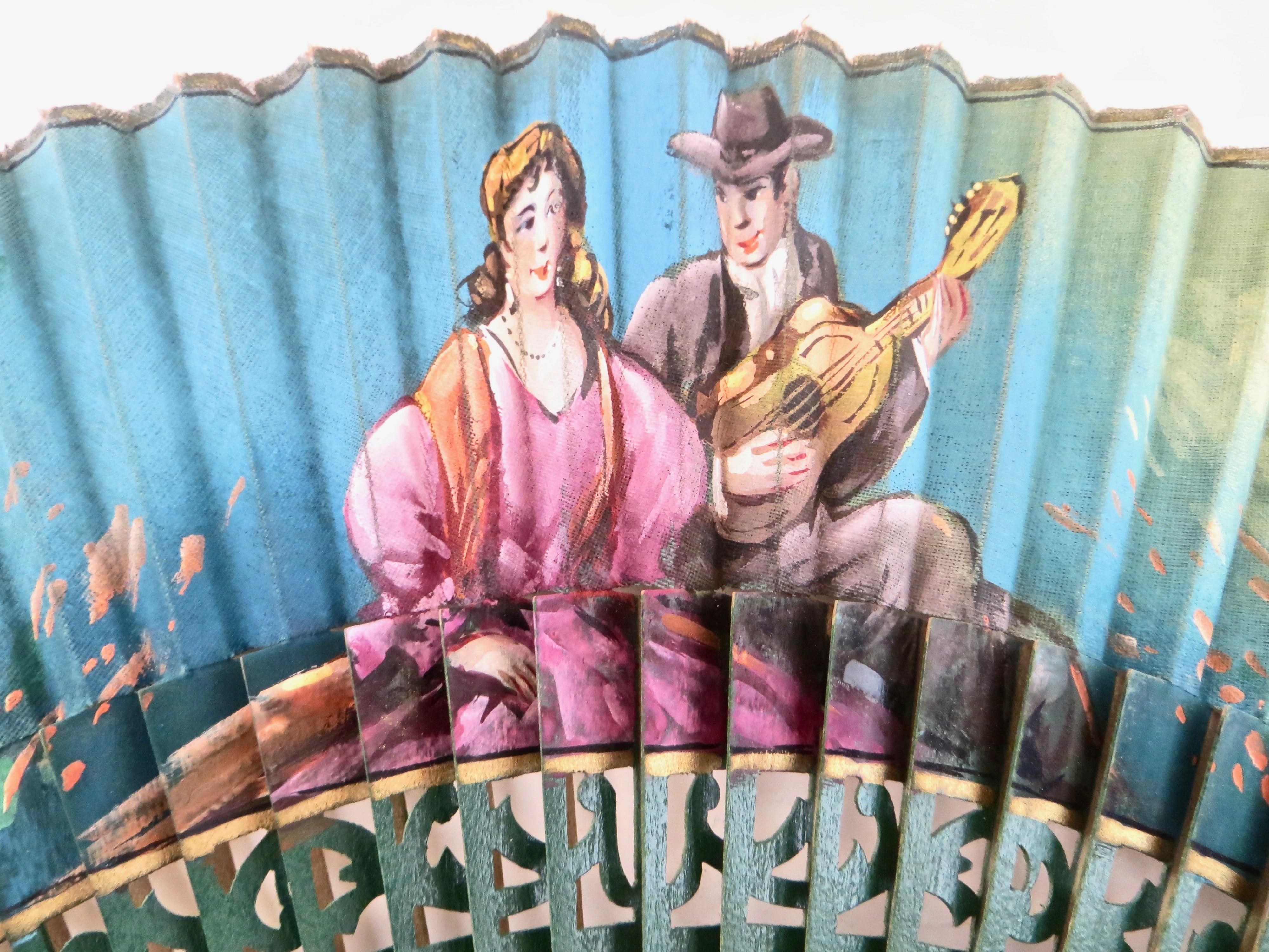 Post War hand held fan, hand painted scenes on green fabric and painted wood. Subject matter on one side consists of a young couple with a gentleman playing guitar serenading the colorfully dressed woman. Floral decorations flank each side, while