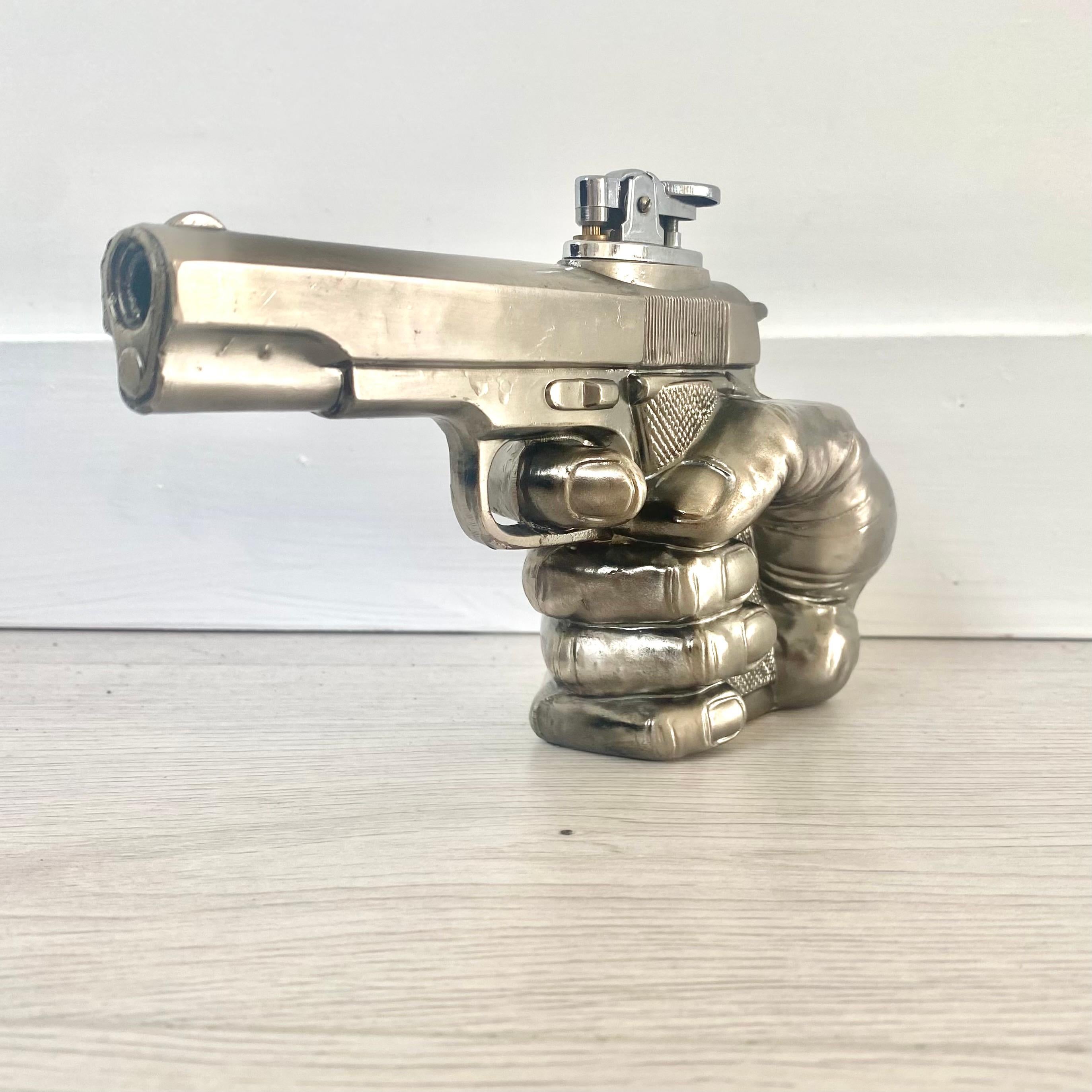 Cool vintage table lighter in the shape of a hand gripping a handgun. Made in Japan. Made of metal and stands up on its own.  Light patina give this piece a great vintage look while still preserving the 80's futuristic chrome finish. Cool tobacco
