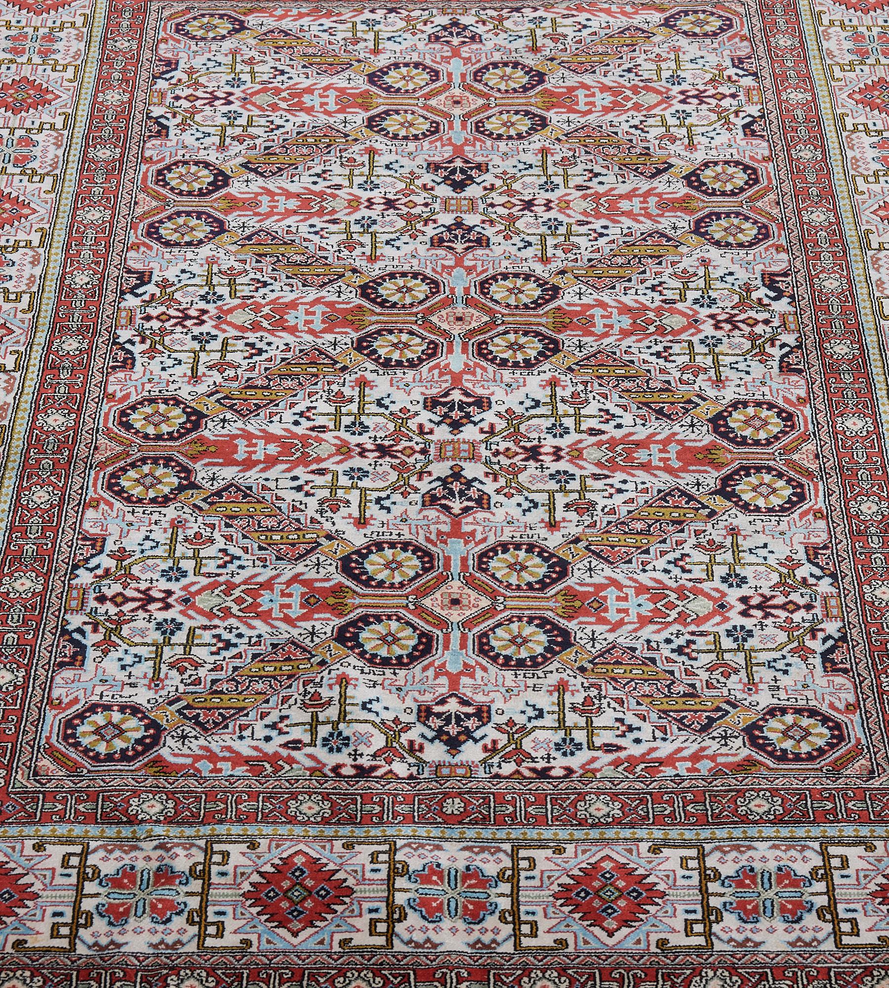 This vintage, circa 1970s, pure silk Qum rug has an ivory field with a dense angular polychrome floral vine around a column of gold panels terminating in paired indigo-blue octogen panels forming open lozenges with tomato-red hooked panels issuing